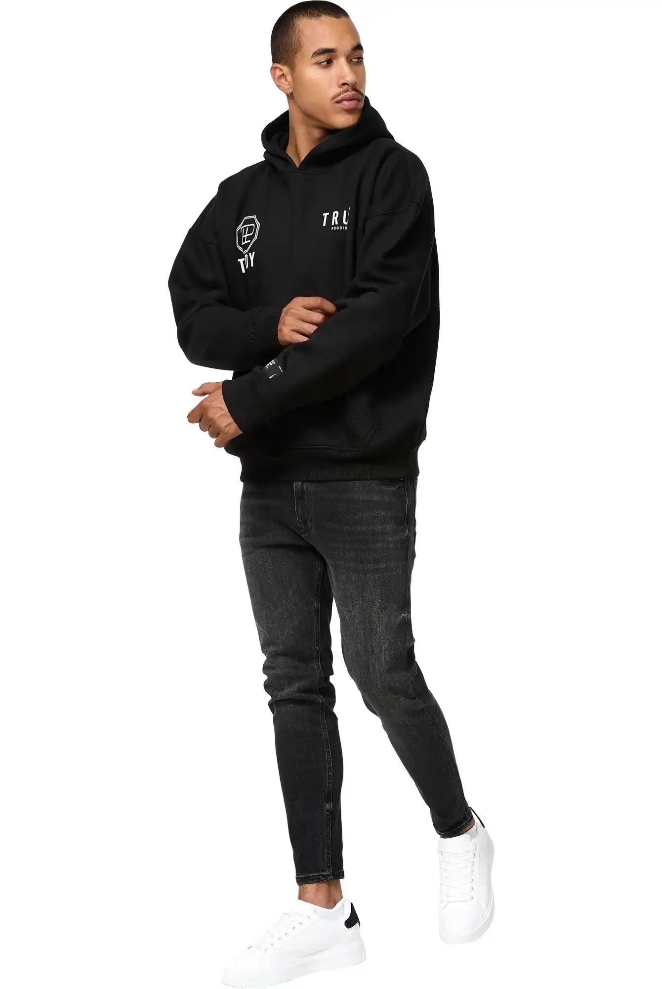 Ein Mann in einem trueprodigy Aaren Oversized Hoodie mit Print, schwarzen Skinny Jeans und weißen Sneakers steht vor einem schlichten weißen Hintergrund.