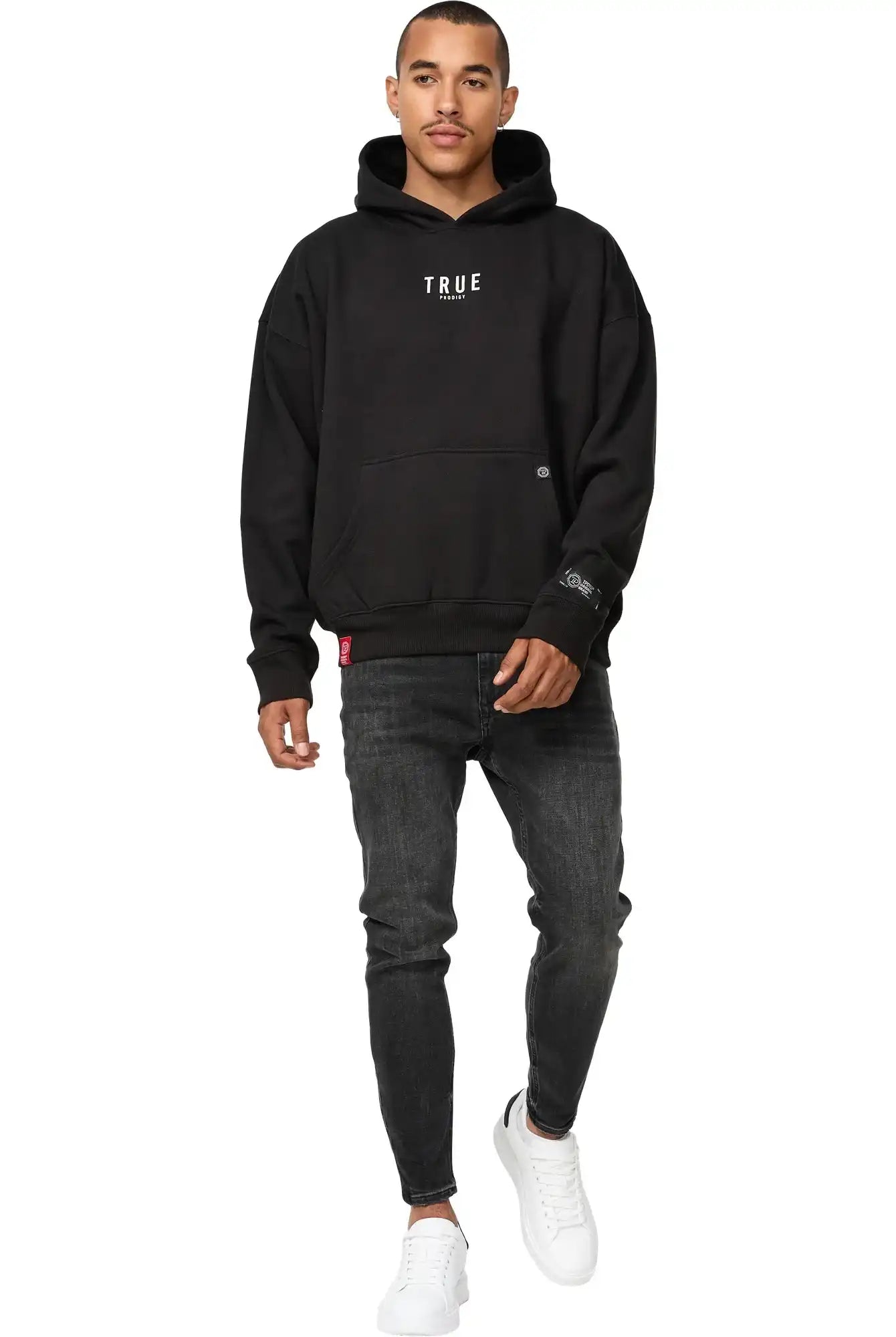 Ein Mann sieht nach vorne und trägt einen schwarzen trueprodigy Quinn Oversized Hoodie mit Print, dunkle Jeans und weiße Turnschuhe vor einem schlichten weißen Hintergrund.
