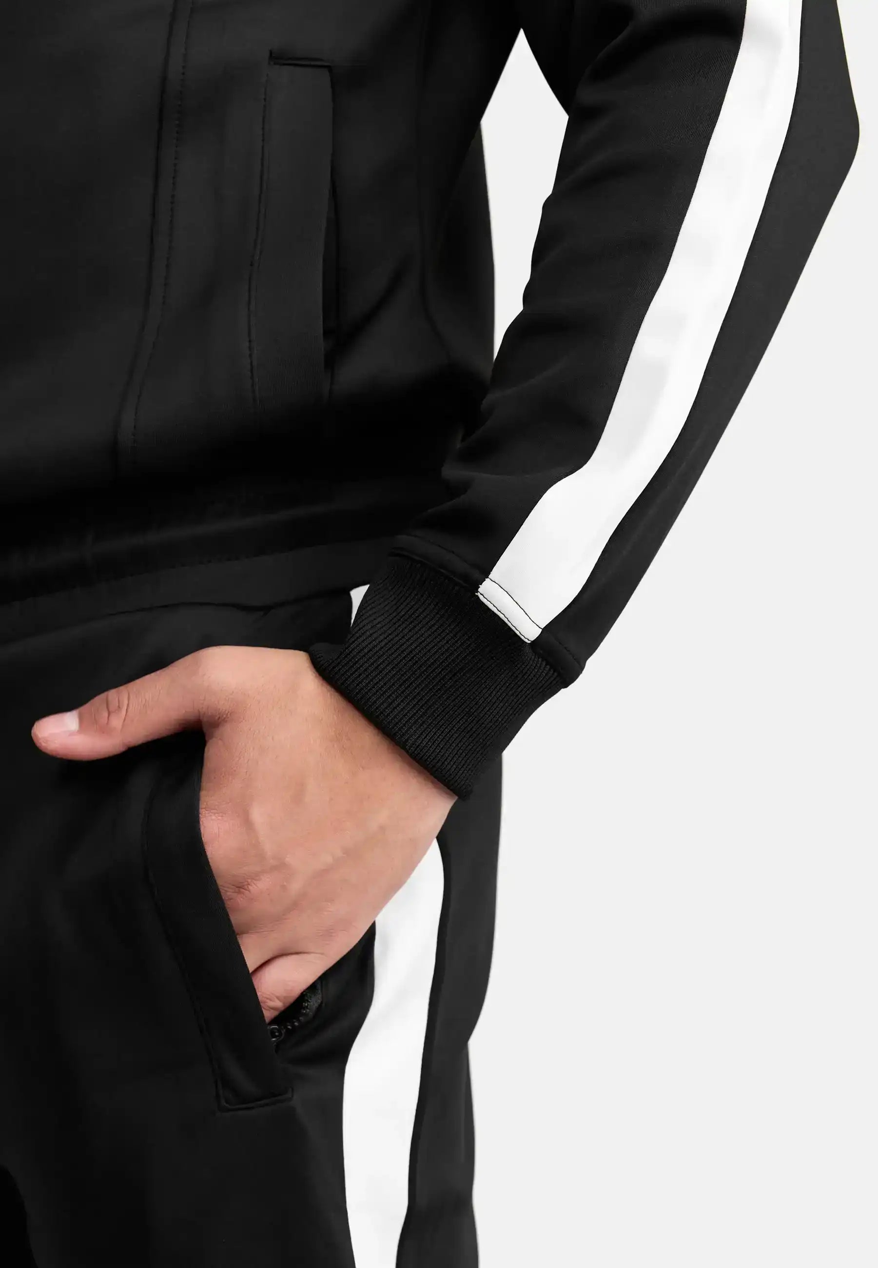 Eine Person, die das trueprodigy Owen Sweatshirt mit Reißverschluss in Schwarz mit weißen Streifen an den Ärmeln und Hosenbeinen trägt, hat die linke Hand in der Tasche und steht vor einem schlichten weißen Hintergrund.