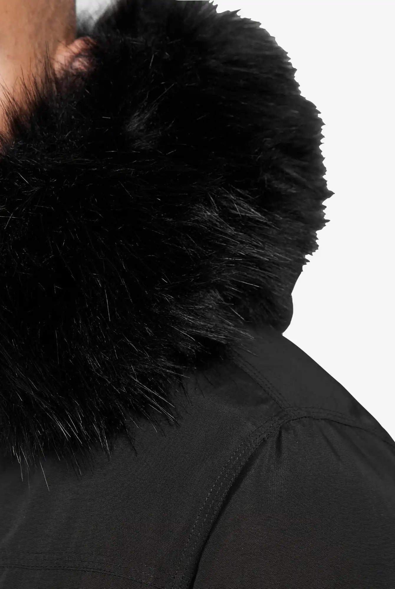 Nahaufnahme einer Person, die die Trueprodigy Noah Winterparka mit Kapuze und Kunstfell in Schwarz trägt. Nur ein Teil des Gesichts und der Schulter sind vor dem einfarbig weißen Hintergrund zu sehen. Der Parka hat einen großen, flauschigen Kunstfellbesatz und eine abnehmbare Kapuze.