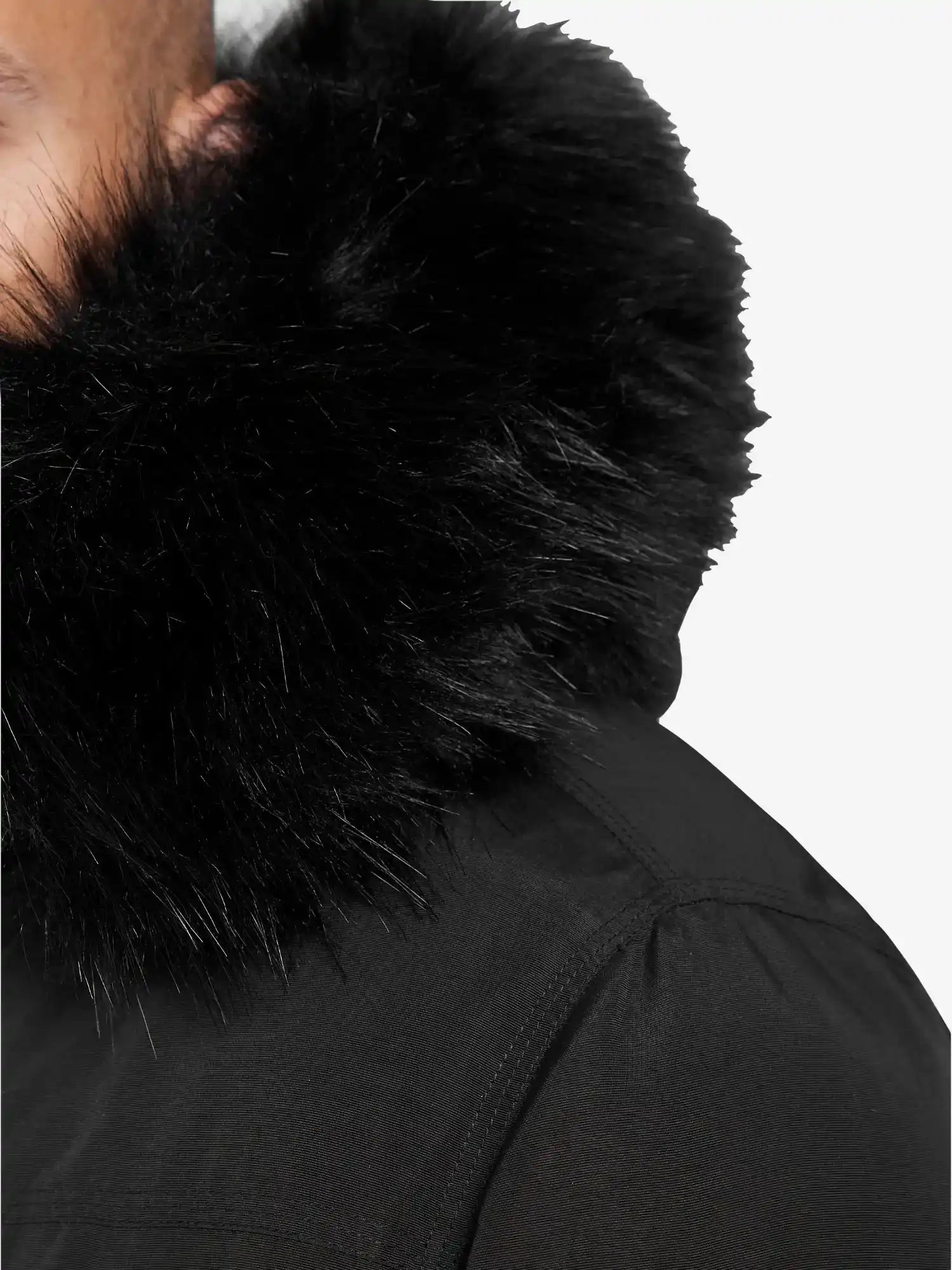 Nahaufnahme einer Person, die die Trueprodigy Noah Winterparka mit Kapuze und Kunstfell in Schwarz trägt. Nur ein Teil des Gesichts und der Schulter sind vor dem einfarbig weißen Hintergrund zu sehen. Der Parka hat einen großen, flauschigen Kunstfellbesatz und eine abnehmbare Kapuze.
