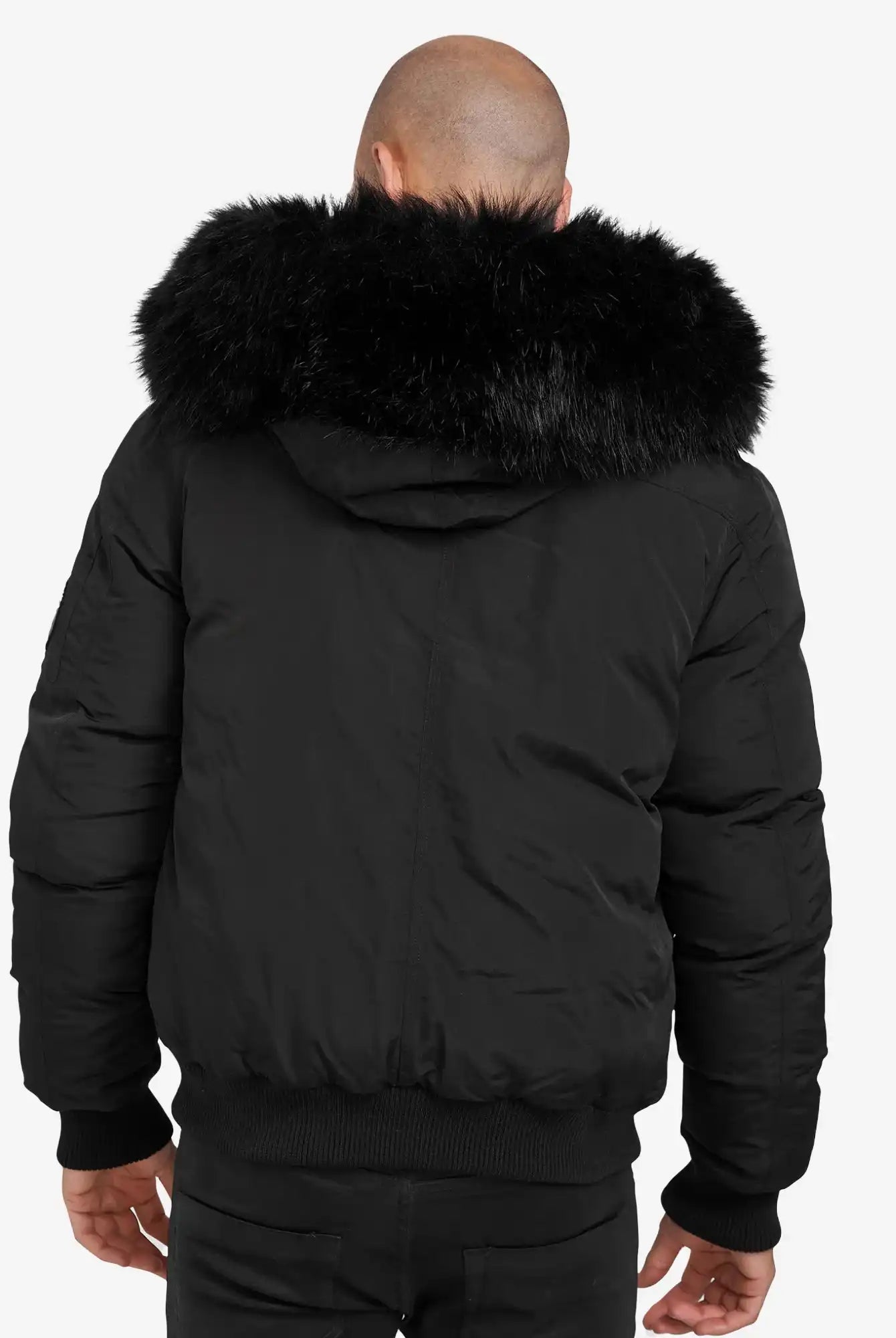 Man sieht eine Person von hinten, die den Noah Winterparka mit Kapuze und Kunstfell von trueprodigy trägt. Die große Kapuze mit Kunstfellbesatz umrahmt ihren kahlen Kopf, während sie entspannt vor einem schlichten weißen Hintergrund steht.