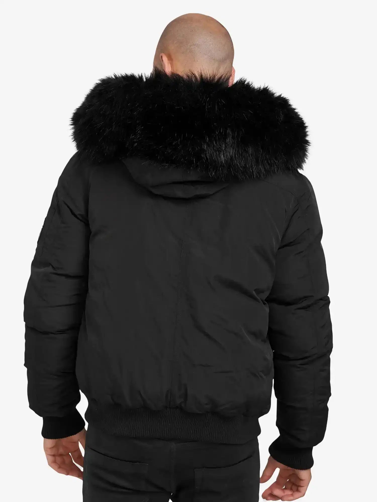 Man sieht eine Person von hinten, die den Noah Winterparka mit Kapuze und Kunstfell von trueprodigy trägt. Die große Kapuze mit Kunstfellbesatz umrahmt ihren kahlen Kopf, während sie entspannt vor einem schlichten weißen Hintergrund steht.