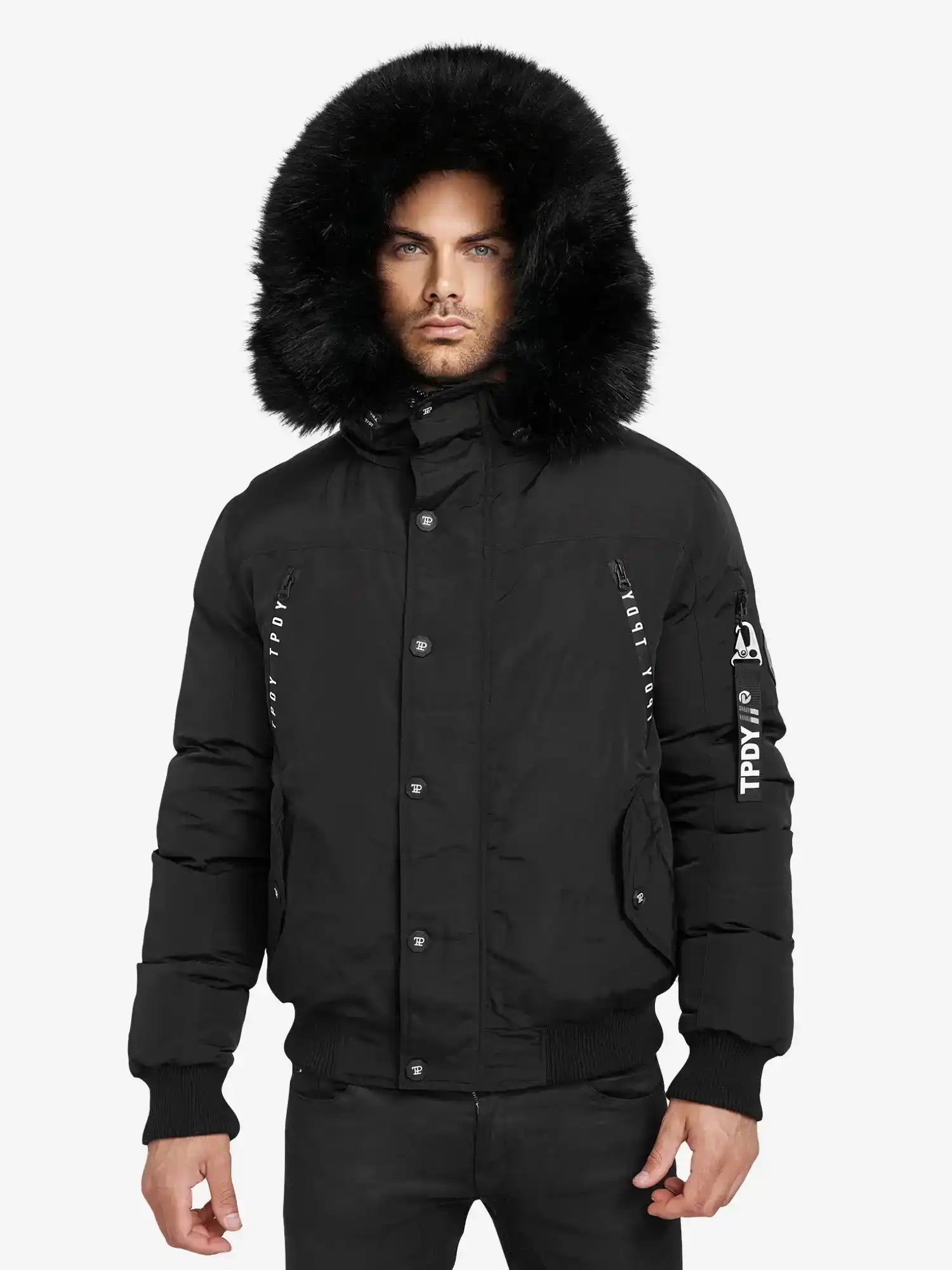 Eine Person, die den Trueprodigy Noah Winterparka mit Kapuze und Kunstfell in Schwarz mit sichtbaren Knöpfen und einem Textpatch auf dem linken Ärmel trägt, steht vor einem schlichten weißen Hintergrund.