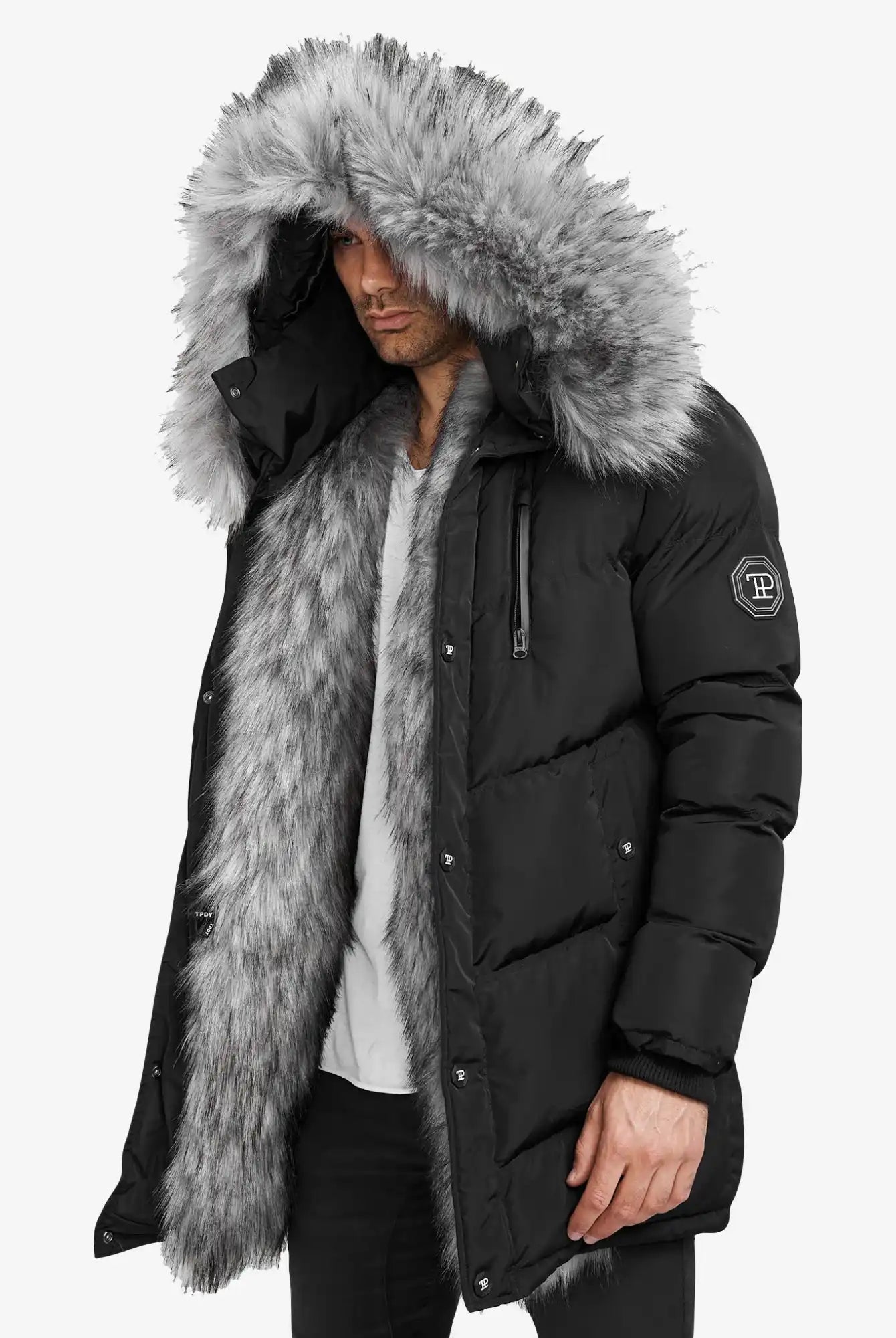 Ein Mann trägt die Zayn Winterjacke mit Kunstfell von trueprodigy, einen schwarzen, wasserabweisenden Herrenparka mit einem großen grauen Kunstfell-Kapuzenbesatz, Logo-Patch am Ärmel, vor einem schlichten weißen Hintergrund.