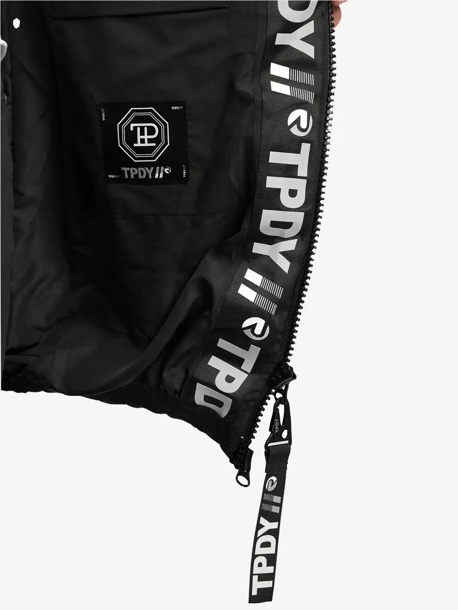 Nahaufnahme der Innenseite der Logan Pufferjacke mit Logo von trueprodigy. Hervorzuheben sind ein Reißverschluss, eine Tasche mit sechseckigem Logoaufnäher und wiederholter weißer TPDY-Text und -Symbole entlang der Innenverkleidung und des Reißverschlusses.