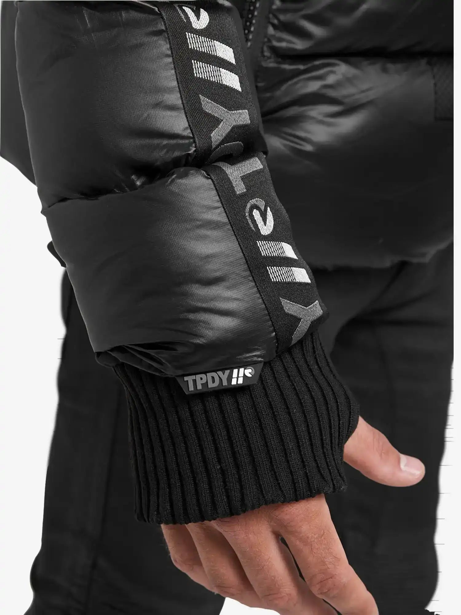 Eine Nahaufnahme einer Hand, die die trueprodigy Logan Pufferjacke mit Logo trägt, zeigt Rippstrickbündchen und einen aufgedruckten weißen Text, darunter TPDY und stilisierte Symbole, auf dem Ärmel.