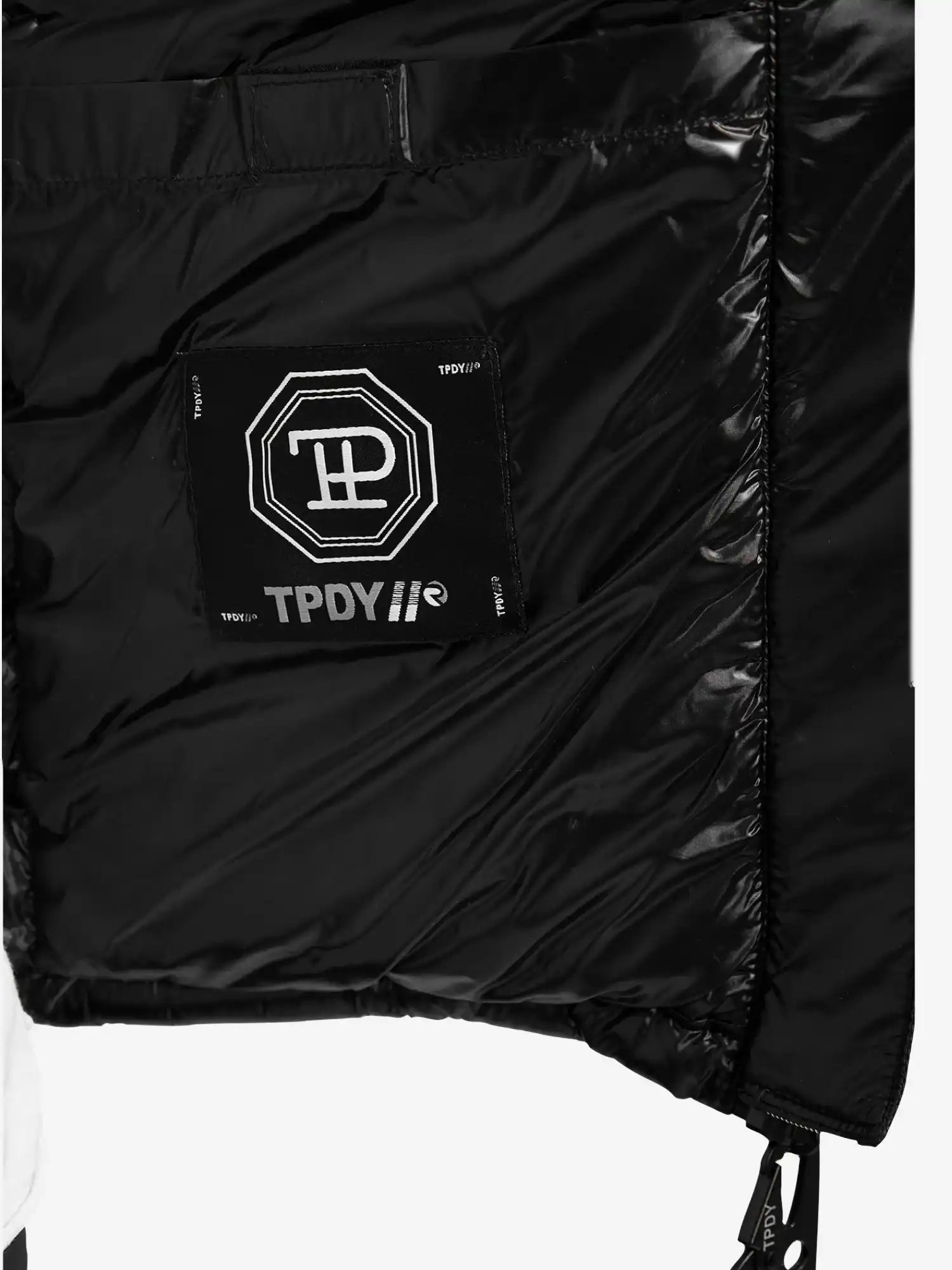 Nahaufnahme der Innenseite der glänzenden, wasserabweisenden trueprodigy Adan Steppjacke mit Kapuze, die einen aufgenähten schwarzen Aufnäher mit weißen geometrischen und TPDY-Textmotiven zeigt. Die gesteppte Textur und die Kapuze sorgen für Stil.