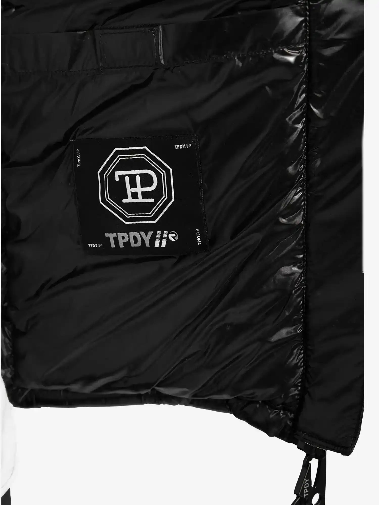 Nahaufnahme der Innenseite der glänzenden, wasserabweisenden trueprodigy Adan Steppjacke mit Kapuze, die einen aufgenähten schwarzen Aufnäher mit weißen geometrischen und TPDY-Textmotiven zeigt. Die gesteppte Textur und die Kapuze sorgen für Stil.