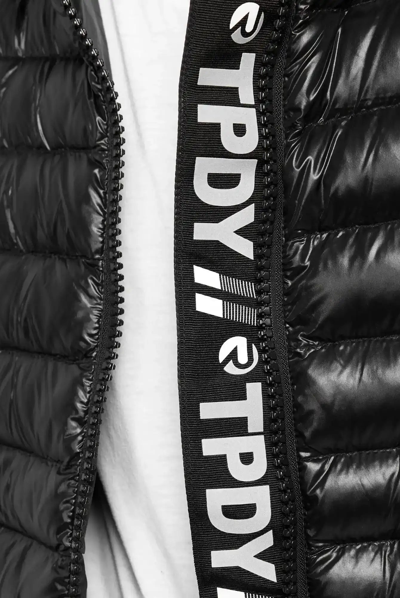 Nahaufnahme der schwarzen, glänzenden Adan Steppjacke mit Kapuze von trueprodigy. Der teilweise geöffnete wasserabweisende Reißverschluss gibt den Blick auf den weißen Stoff darunter frei, und das schwarze Reißverschlussfutter ist mit weißem TPDY-Text und -Logos versehen.