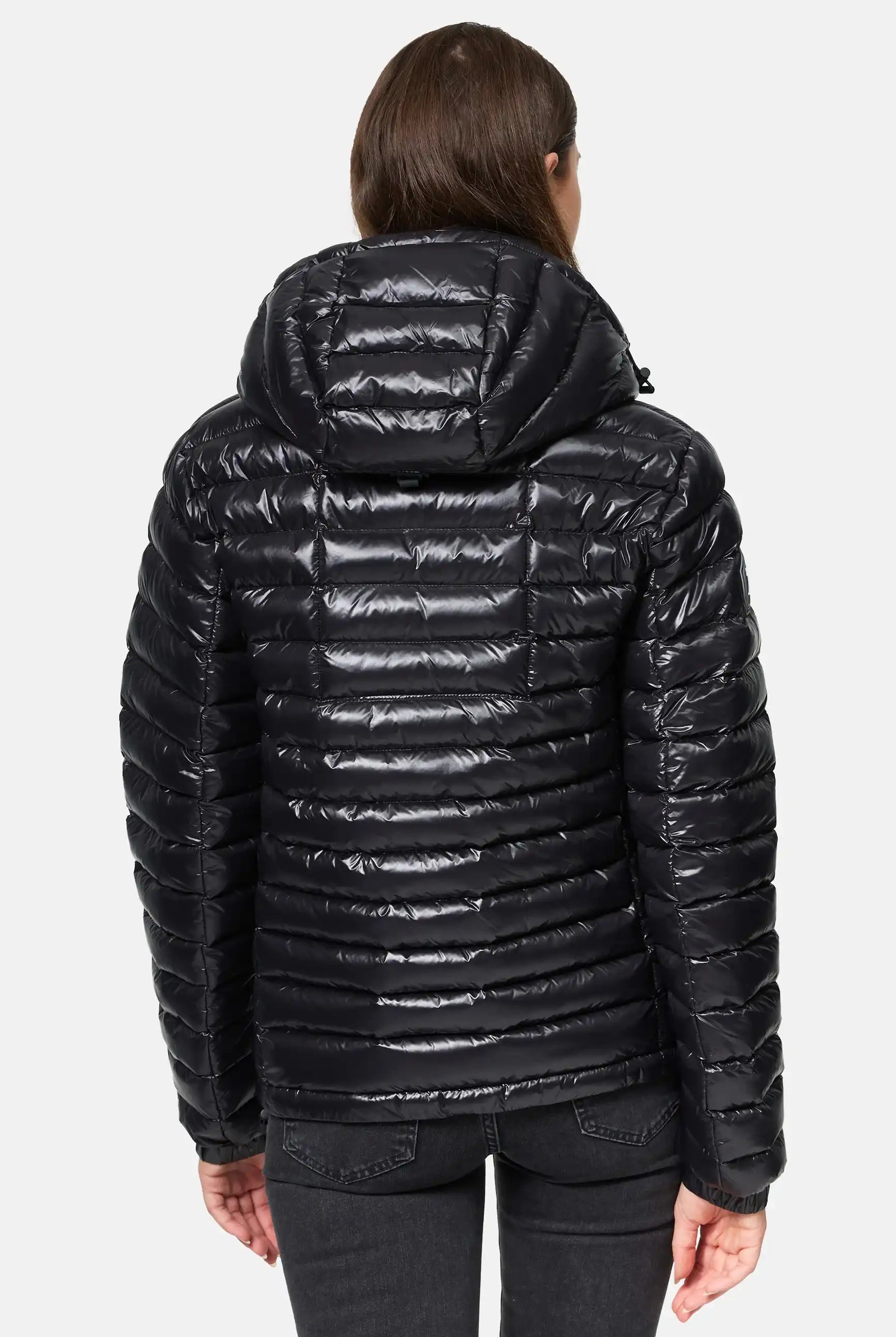 Eine Person mit schulterlangem braunem Haar trägt die glänzende, wasserabweisende Adan F Steppjacke mit Kapuze von trueprodigy. Die Steppjacke hat horizontale Steppnähte und eine Kapuze. Sie schaut von der Kamera weg und trägt eine dunkle Jeans.