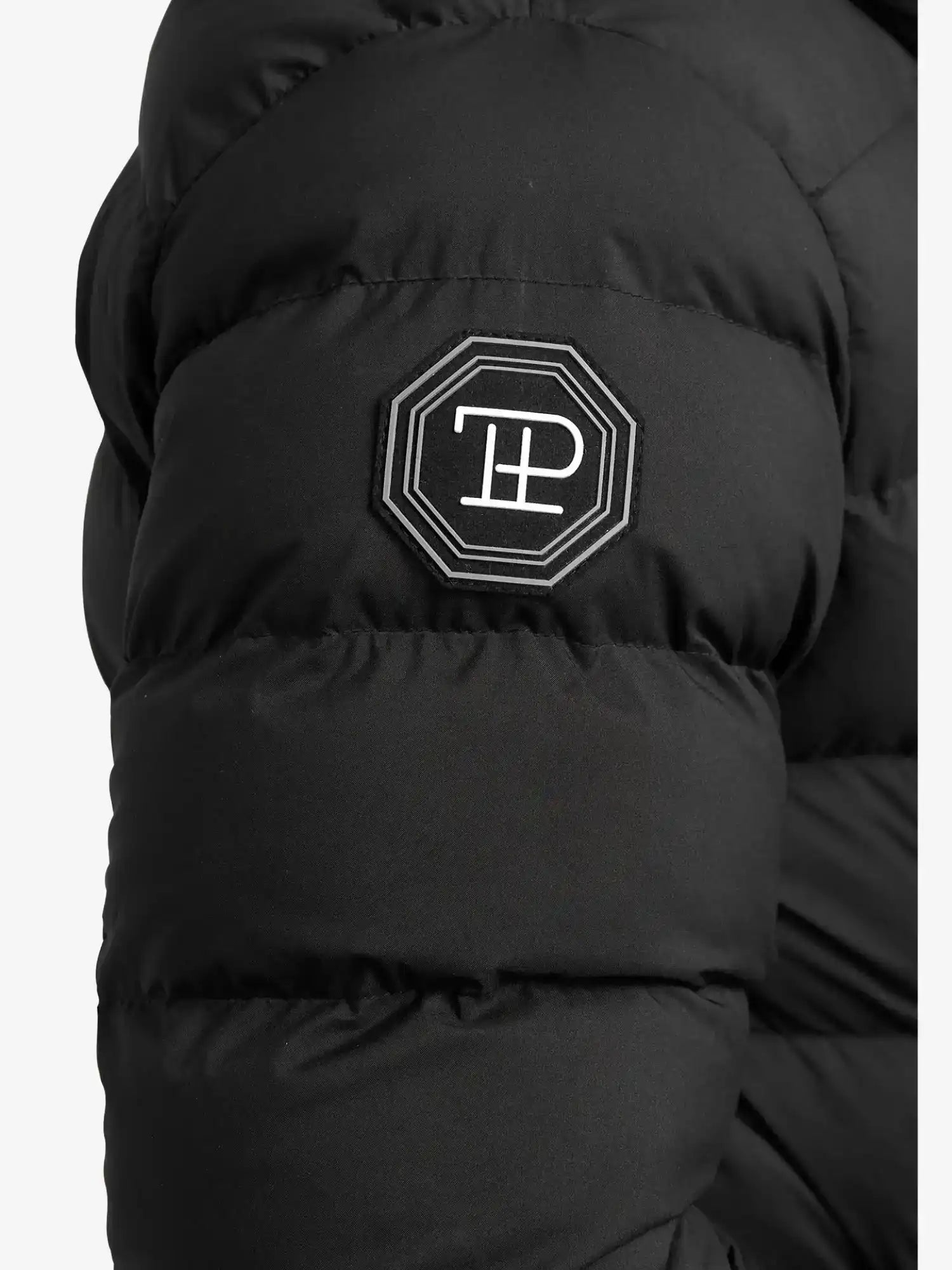 Nahaufnahme der Chester Lange Pufferjacke mit Logo von trueprodigy: ein schwarzer, wasserabweisender Herrenparka mit gestepptem Ärmel und aufgesticktem achteckigen Aufnäher mit weißem T- und P-Logo mit weißem Rand.