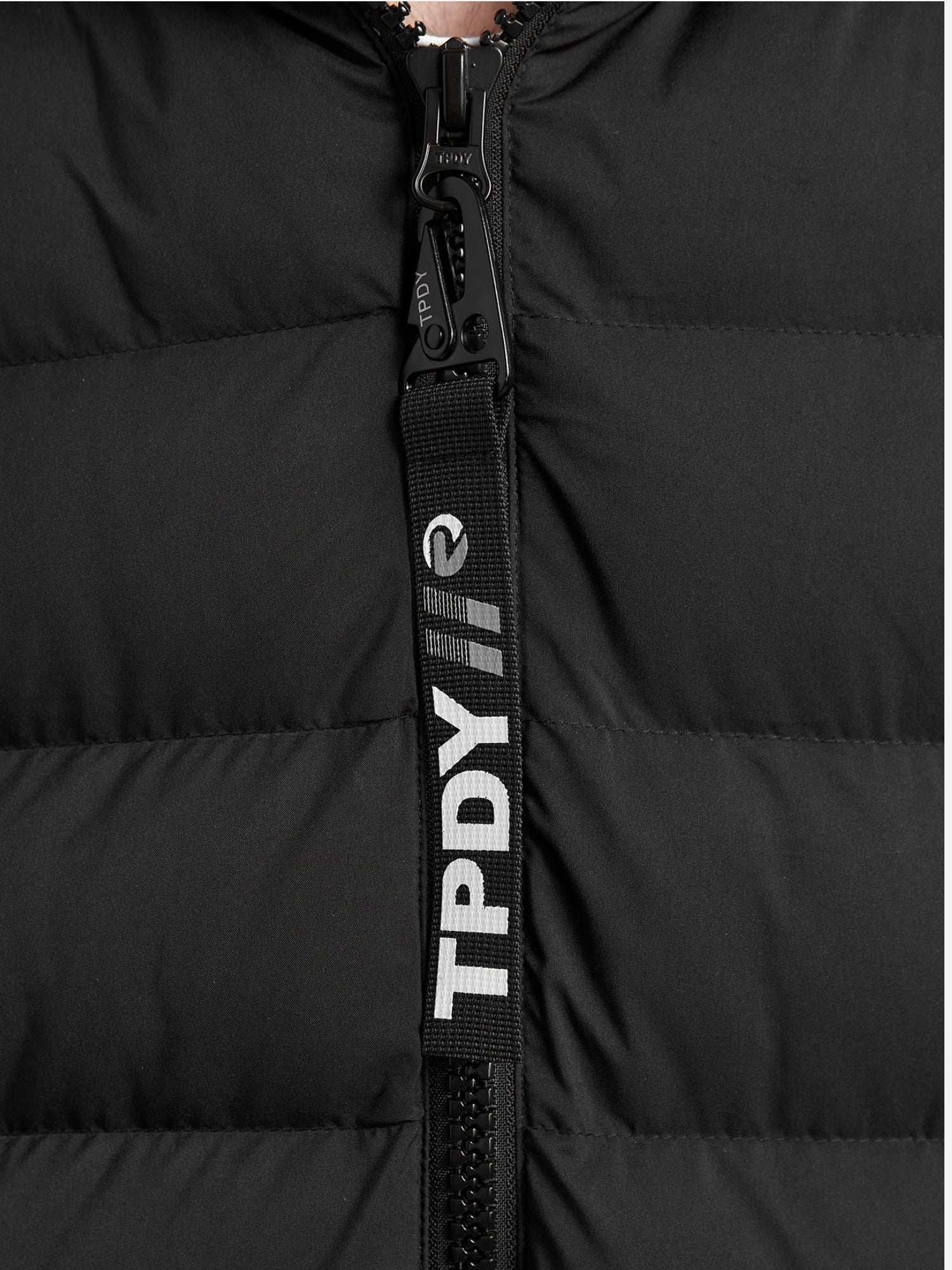 Nahaufnahme der Chester Lange Pufferjacke mit Logo von trueprodigy in Schwarz. Sie zeigt einen markanten Reißverschluss und eine schwarze Zuglasche mit weißem TPDY Schriftzug und Logo. Dieser wasserabweisende Herrenparka vereint Stil und Funktionalität.