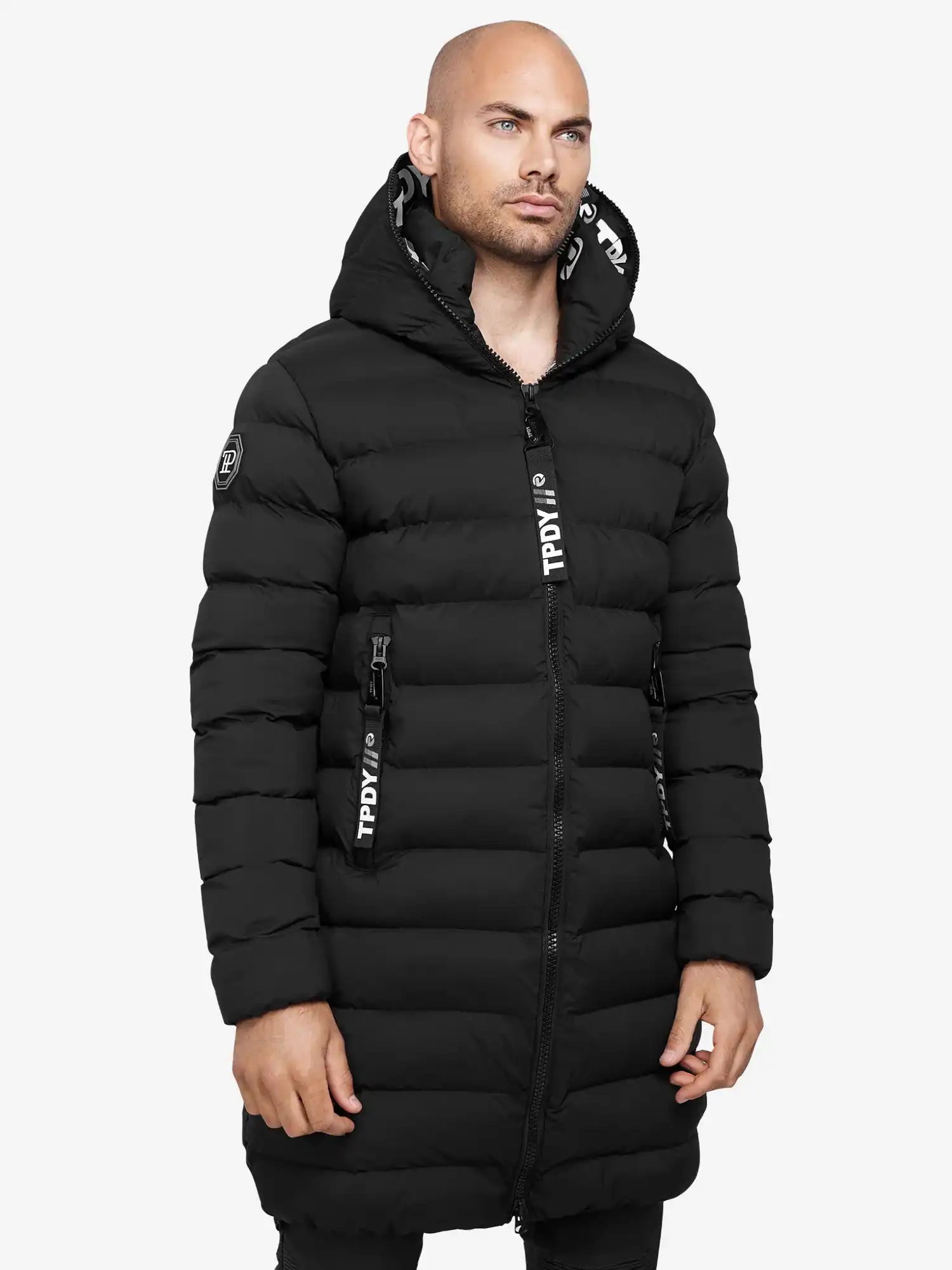 Ein Mann trägt die Chester Lange Pufferjacke mit Logo von trueprodigy im Herrenparka-Stil. Die schwarze, wasserabweisende Jacke hat sichtbare Reißverschlüsse sowie weiße Logodetails an Kapuze und Zipper.
