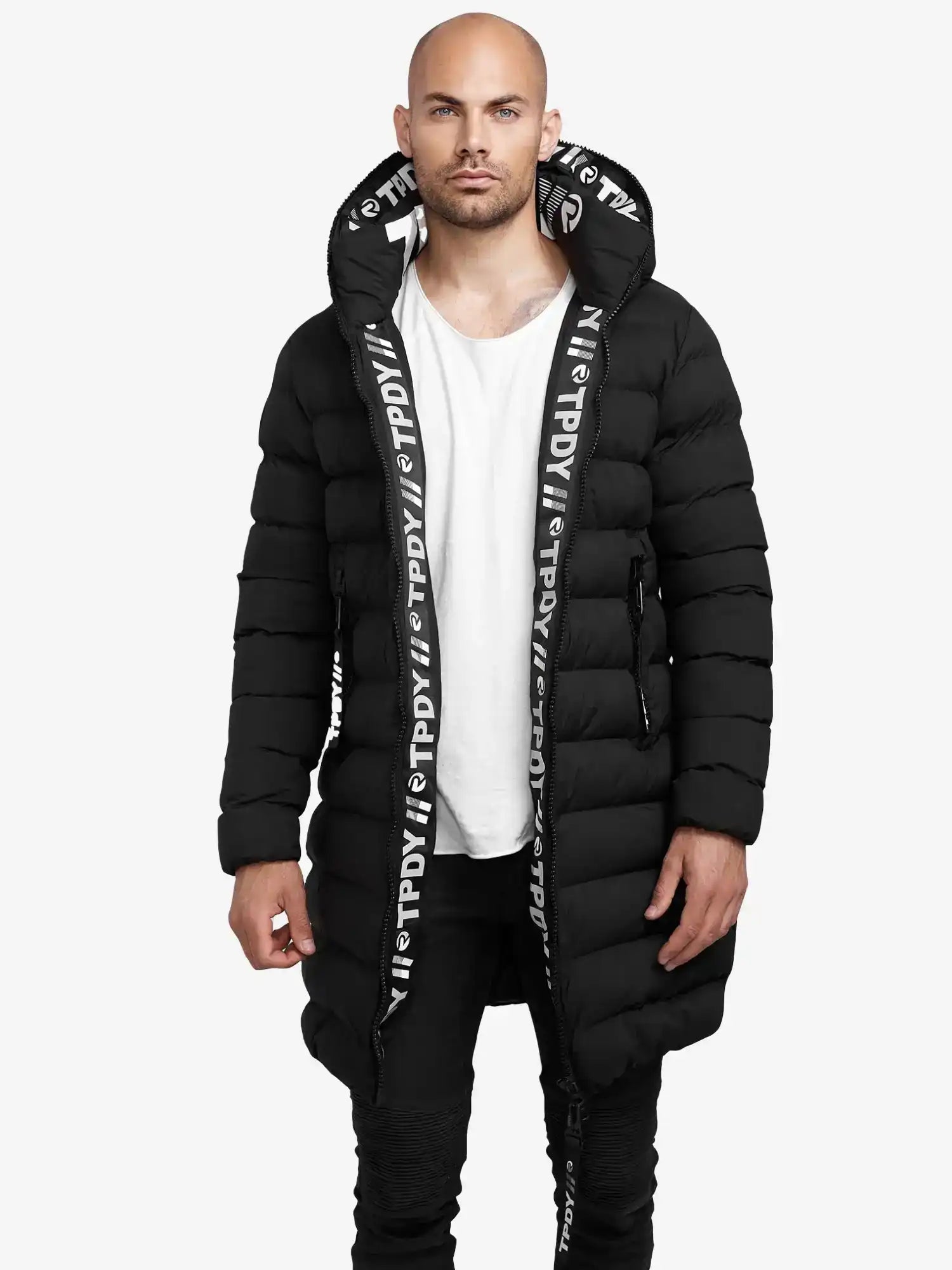 Ein Mann steht vor der Kamera und trägt die trueprodigy Chester Lange Pufferjacke mit Logo mit Kapuze und weißem Logo-Schriftzug am Saum, gepaart mit einem weißen T-Shirt und einer schwarzen Hose vor einem schlichten weißen Hintergrund.