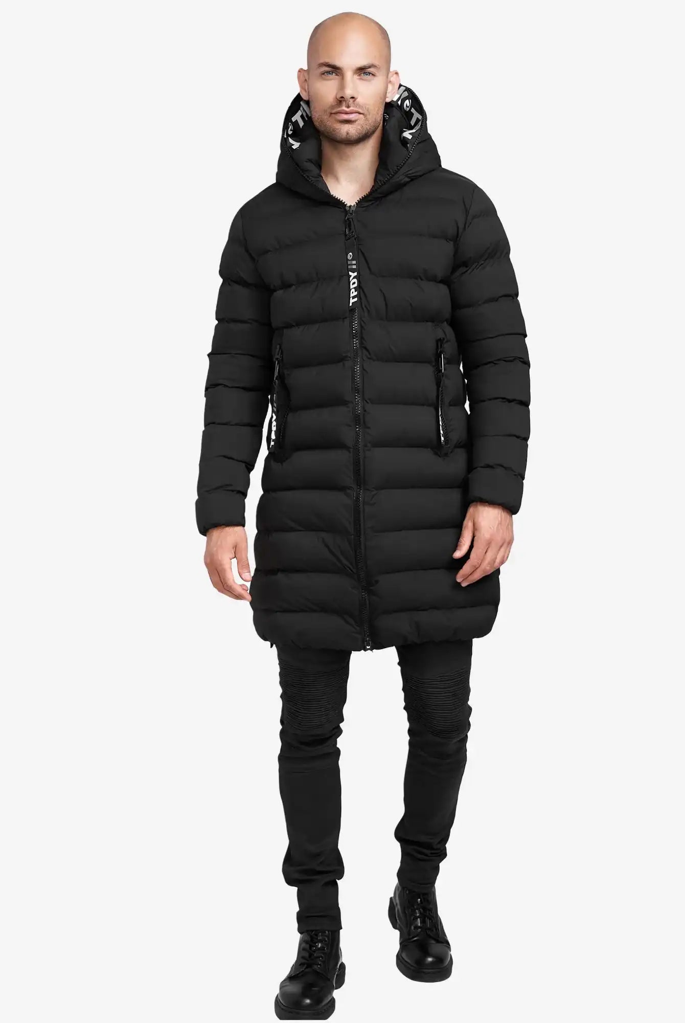 Ein Mann trägt die Chester Lange Pufferjacke mit Logo von trueprodigy, dazu schwarze Hose und Stiefel. Er steht frontal vor einem schlichten weißen Hintergrund.