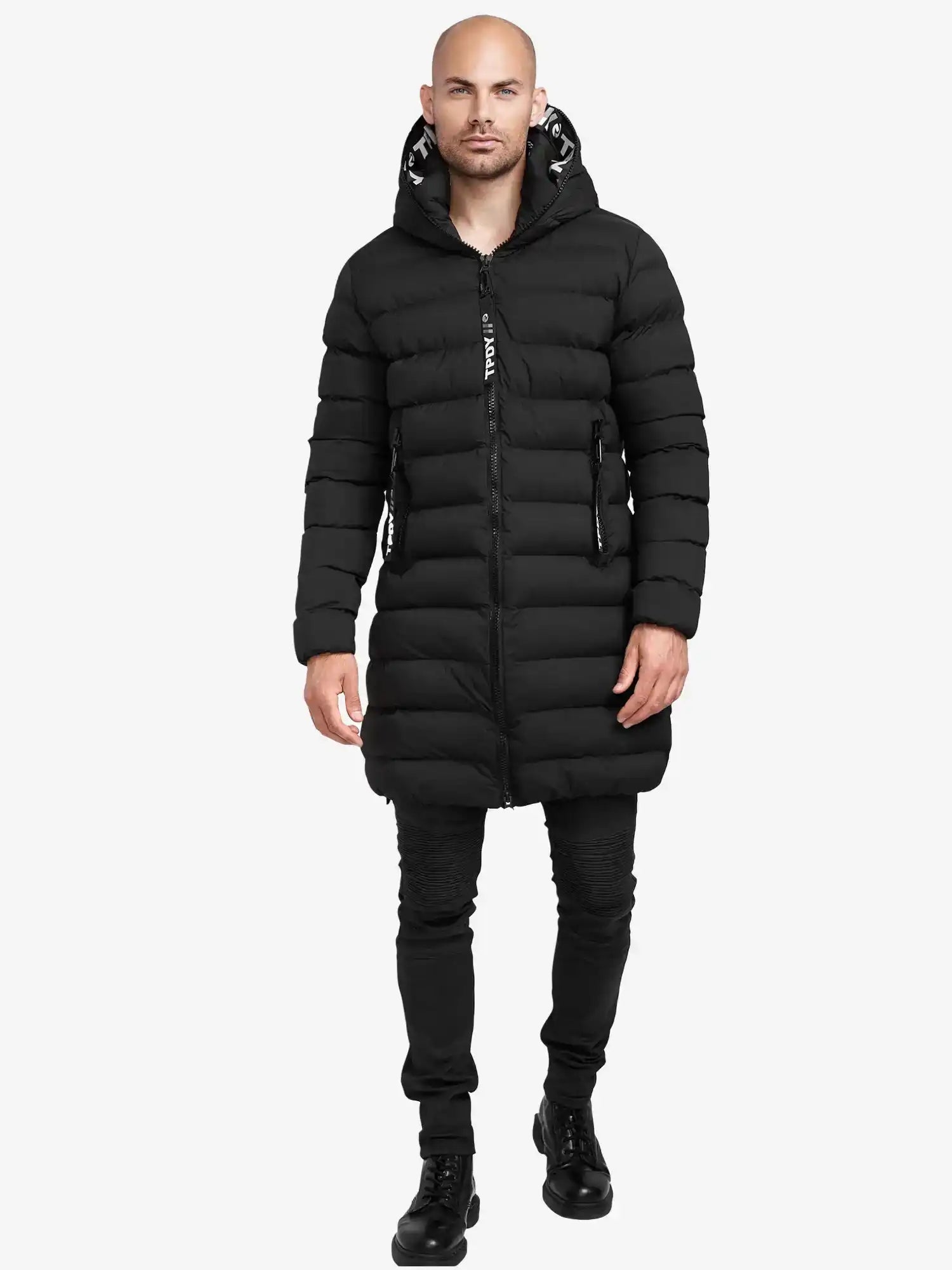 Ein Mann trägt die Chester Lange Pufferjacke mit Logo von trueprodigy, dazu schwarze Hose und Stiefel. Er steht frontal vor einem schlichten weißen Hintergrund.