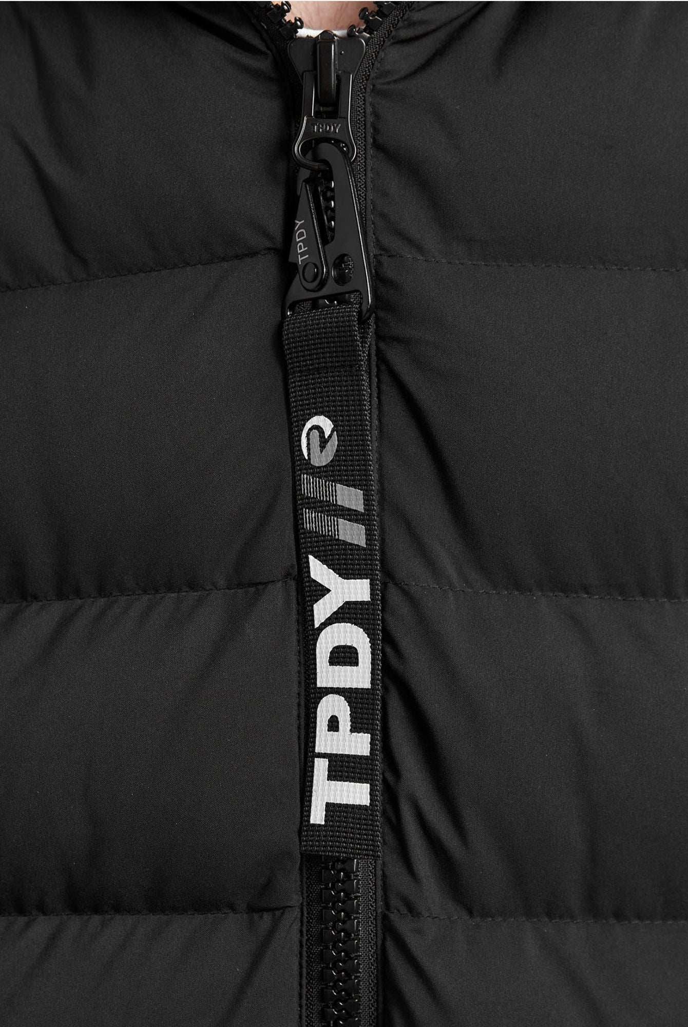 Nahaufnahme der Chester F Lange Pufferjacke mit Logo von trueprodigy: Die gesteppte Jacke hat einen sichtbaren Reißverschluss mit schwarzer Zuglasche und weißem "TPDY"-Schriftzug und Logo. Dieser Damenparka ist wasserabweisend für stilvollen, praktischen Schutz.