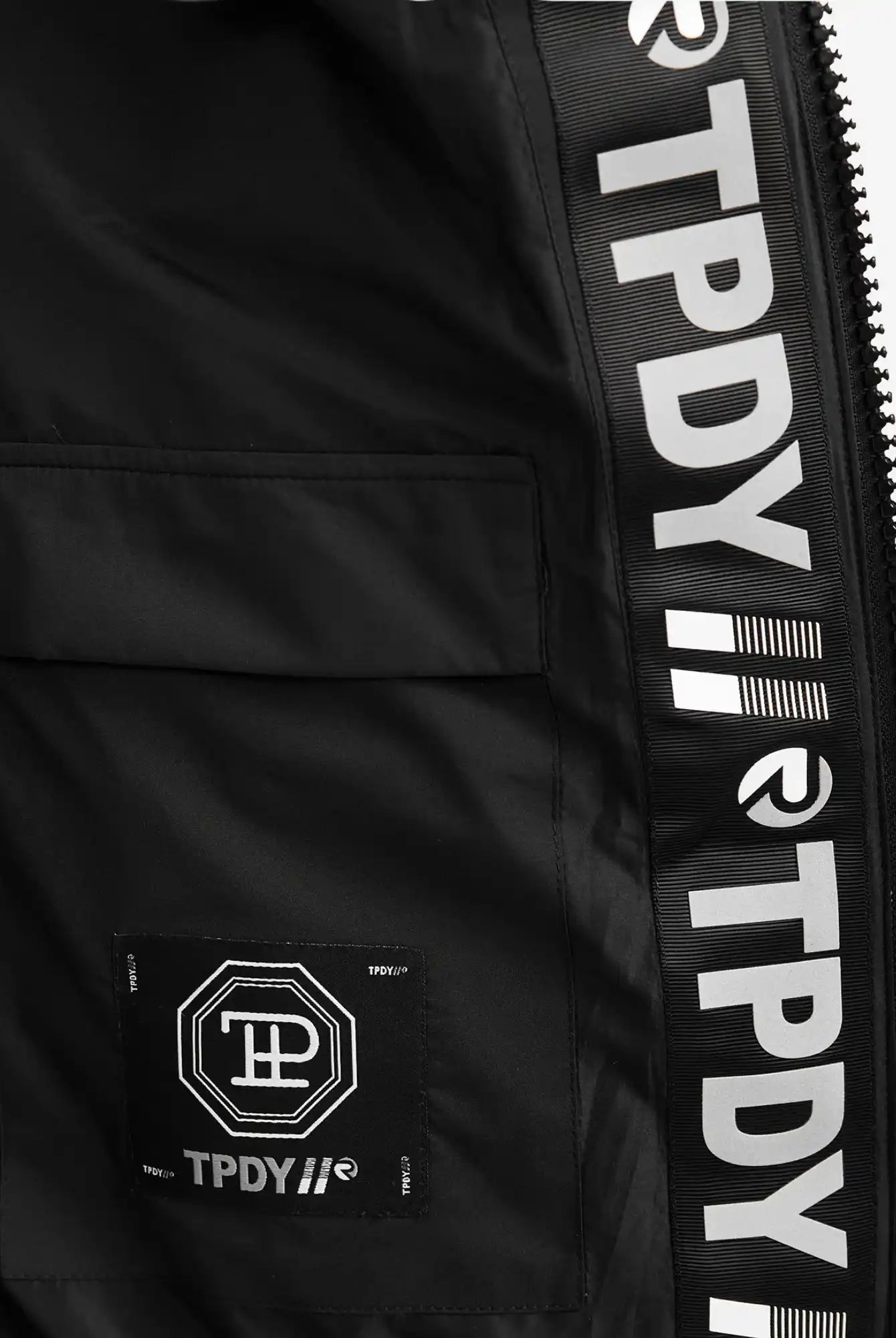 Nahaufnahme der Neo Kurze Pufferjacke mit Logo von trueprodigy: Die wasserabweisende Innenseite offenbart ein geometrisches Stoffetikett mit TPDY-Schriftzug an der Innennaht, sowie eine teilweise sichtbare Kapuze und einen Reißverschluss auf der rechten Seite.