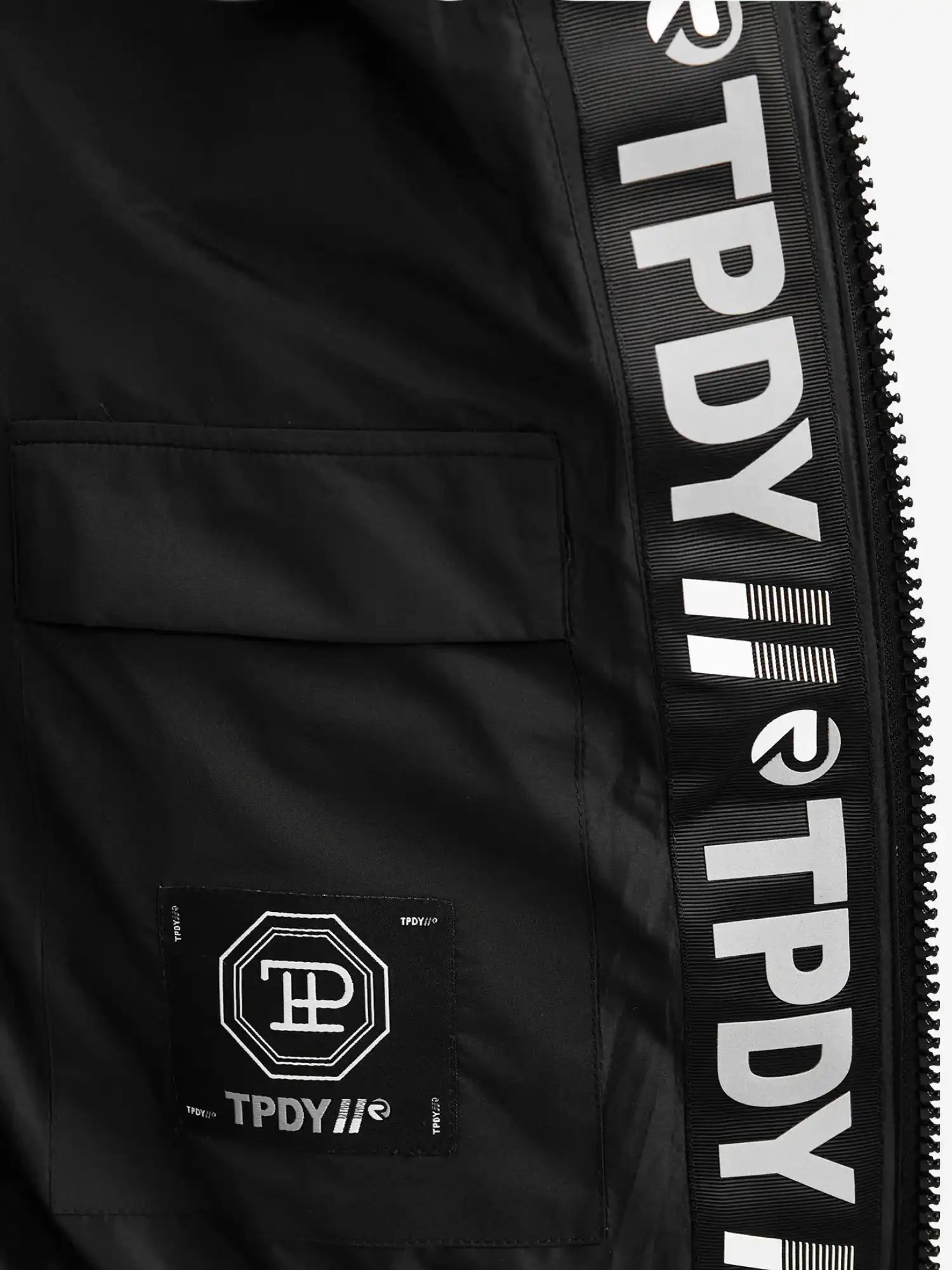 Nahaufnahme der Neo Kurze Pufferjacke mit Logo von trueprodigy: Die wasserabweisende Innenseite offenbart ein geometrisches Stoffetikett mit TPDY-Schriftzug an der Innennaht, sowie eine teilweise sichtbare Kapuze und einen Reißverschluss auf der rechten Seite.