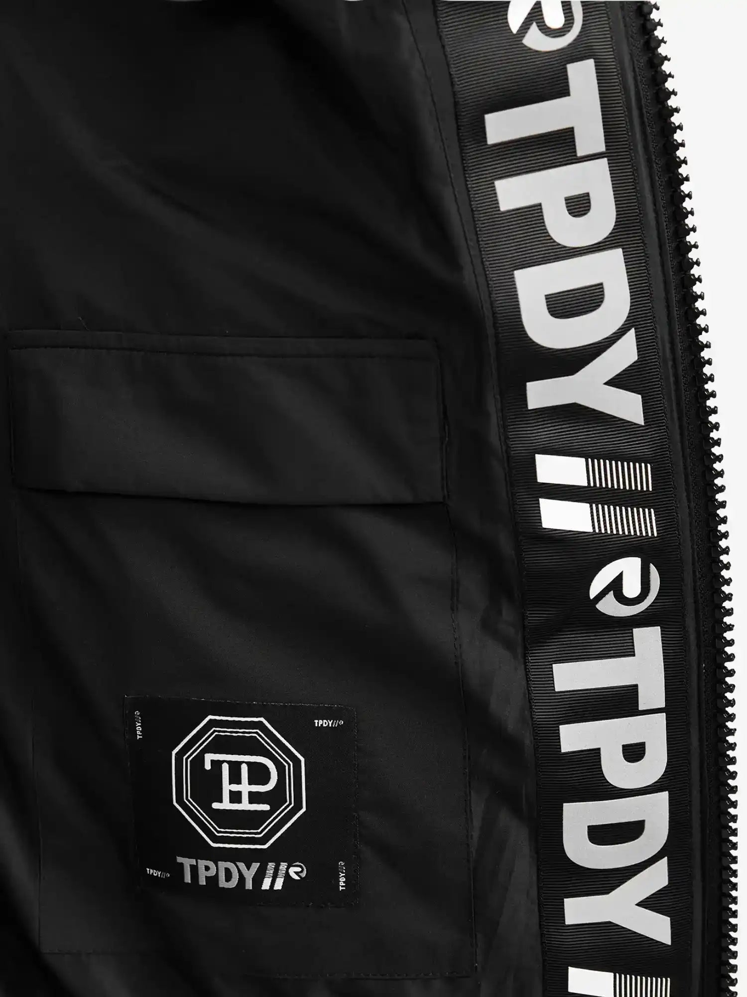 Nahaufnahme der Neo Kurze Pufferjacke mit Logo von trueprodigy: Die wasserabweisende Innenseite offenbart ein geometrisches Stoffetikett mit TPDY-Schriftzug an der Innennaht, sowie eine teilweise sichtbare Kapuze und einen Reißverschluss auf der rechten Seite.