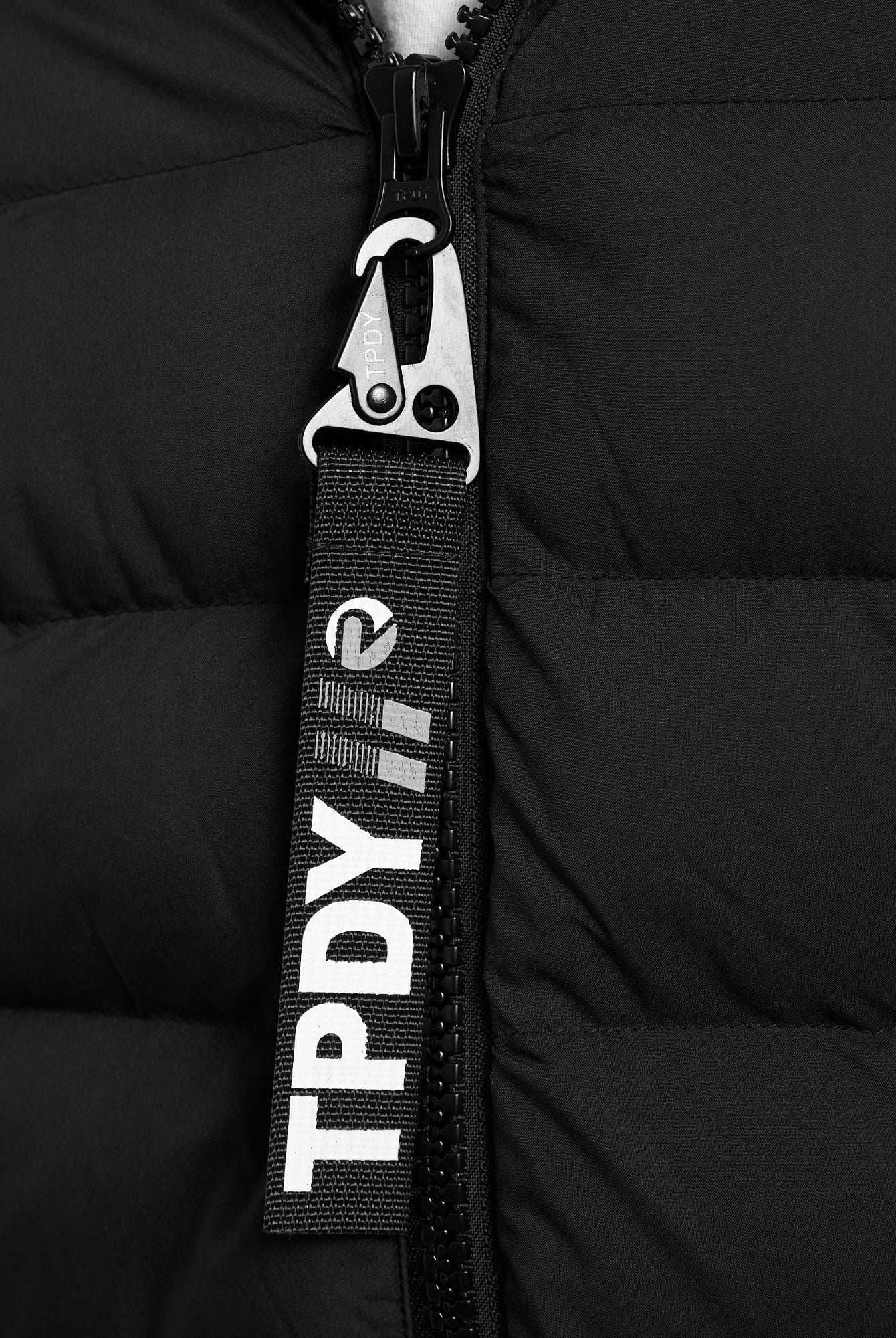 Nahaufnahme der Neo Kurze Pufferjacke mit Logo von trueprodigy: eine schwarze Steppjacke mit Metallreißverschluss und einer schwarzen Stofflasche mit "TPDY" und Logo in Weiß. Diese wasserabweisende Jacke ist ideal für unvorhersehbares Wetter.