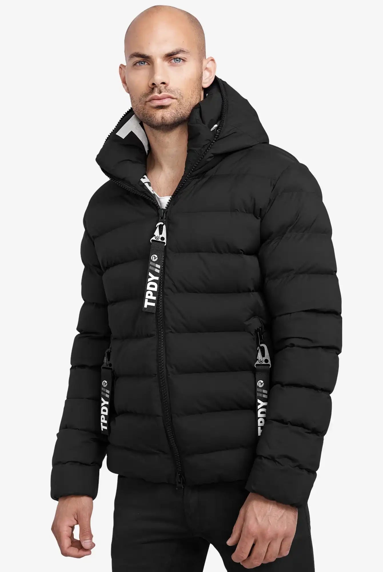 Ein Mann trägt die trueprodigy Neo Kurze Pufferjacke mit Logo, eine schwarze, wasserabweisende Jacke mit Kapuze und horizontalem Steppmuster. Schwarz-weiße Reißverschlüsse vollenden das Design vor weißem Hintergrund.