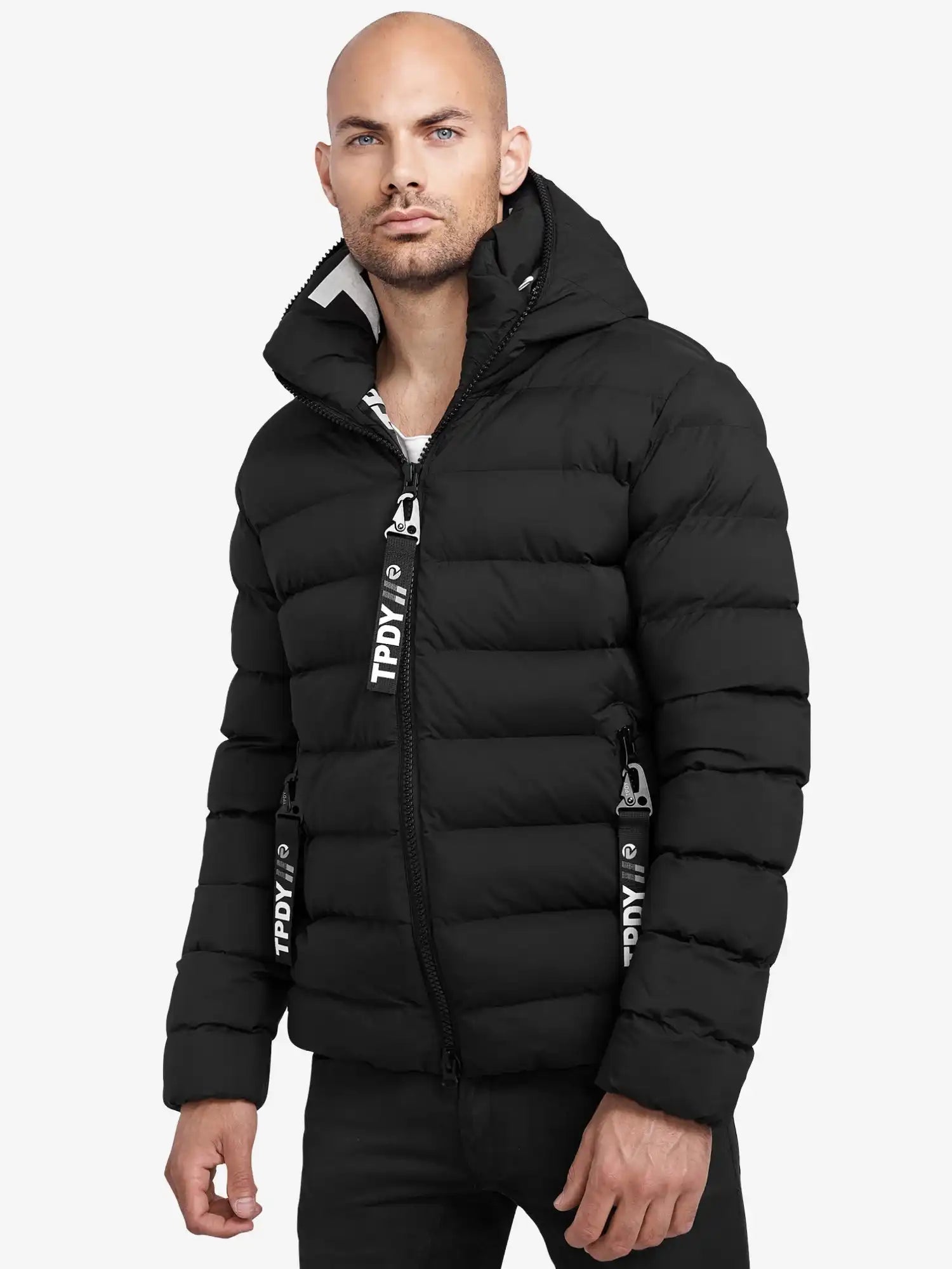 Ein Mann trägt die trueprodigy Neo Kurze Pufferjacke mit Logo, eine schwarze, wasserabweisende Jacke mit Kapuze und horizontalem Steppmuster. Schwarz-weiße Reißverschlüsse vollenden das Design vor weißem Hintergrund.