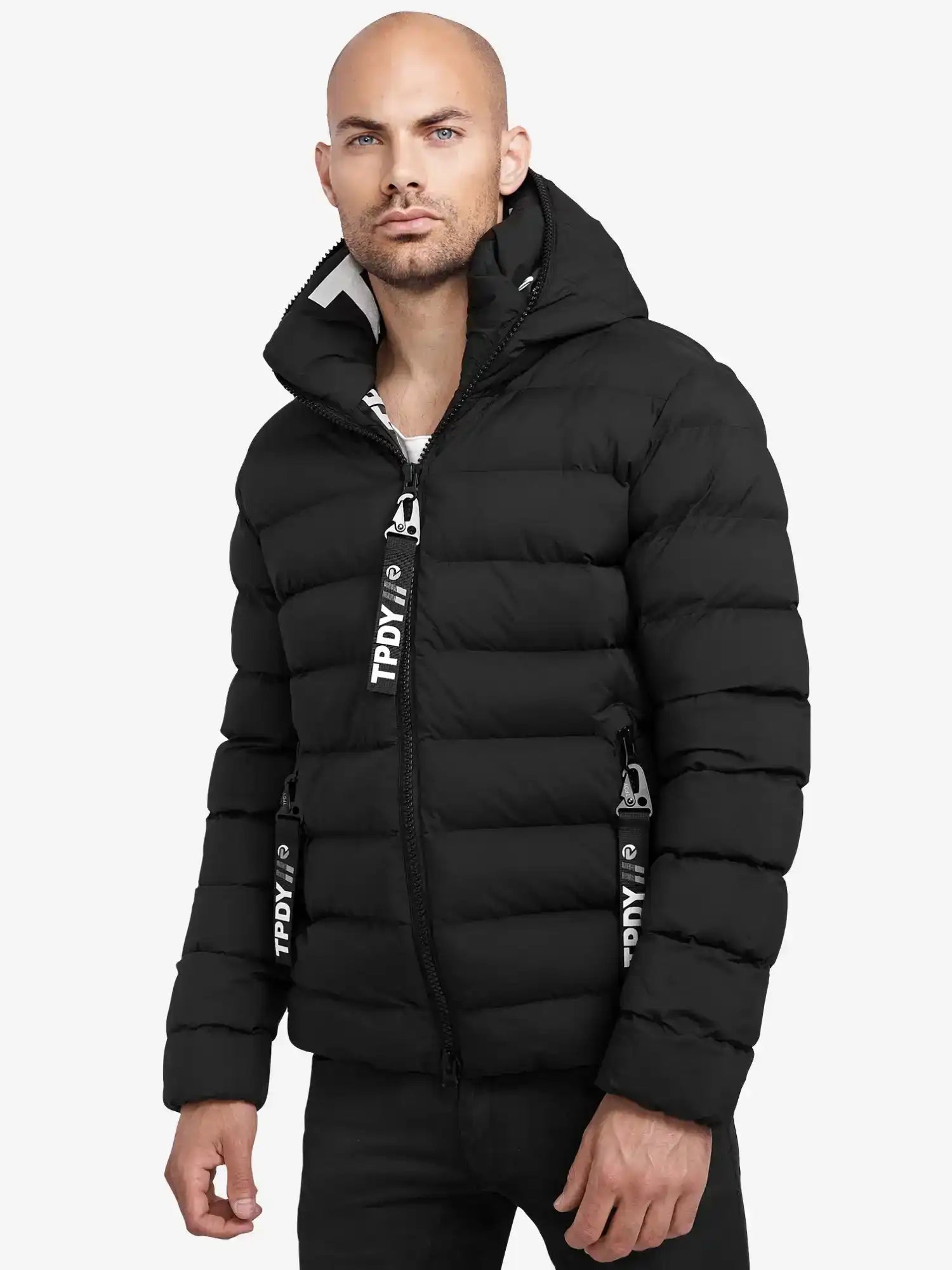 Ein Mann trägt die trueprodigy Neo Kurze Pufferjacke mit Logo, eine schwarze, wasserabweisende Jacke mit Kapuze und horizontalem Steppmuster. Schwarz-weiße Reißverschlüsse vollenden das Design vor weißem Hintergrund.