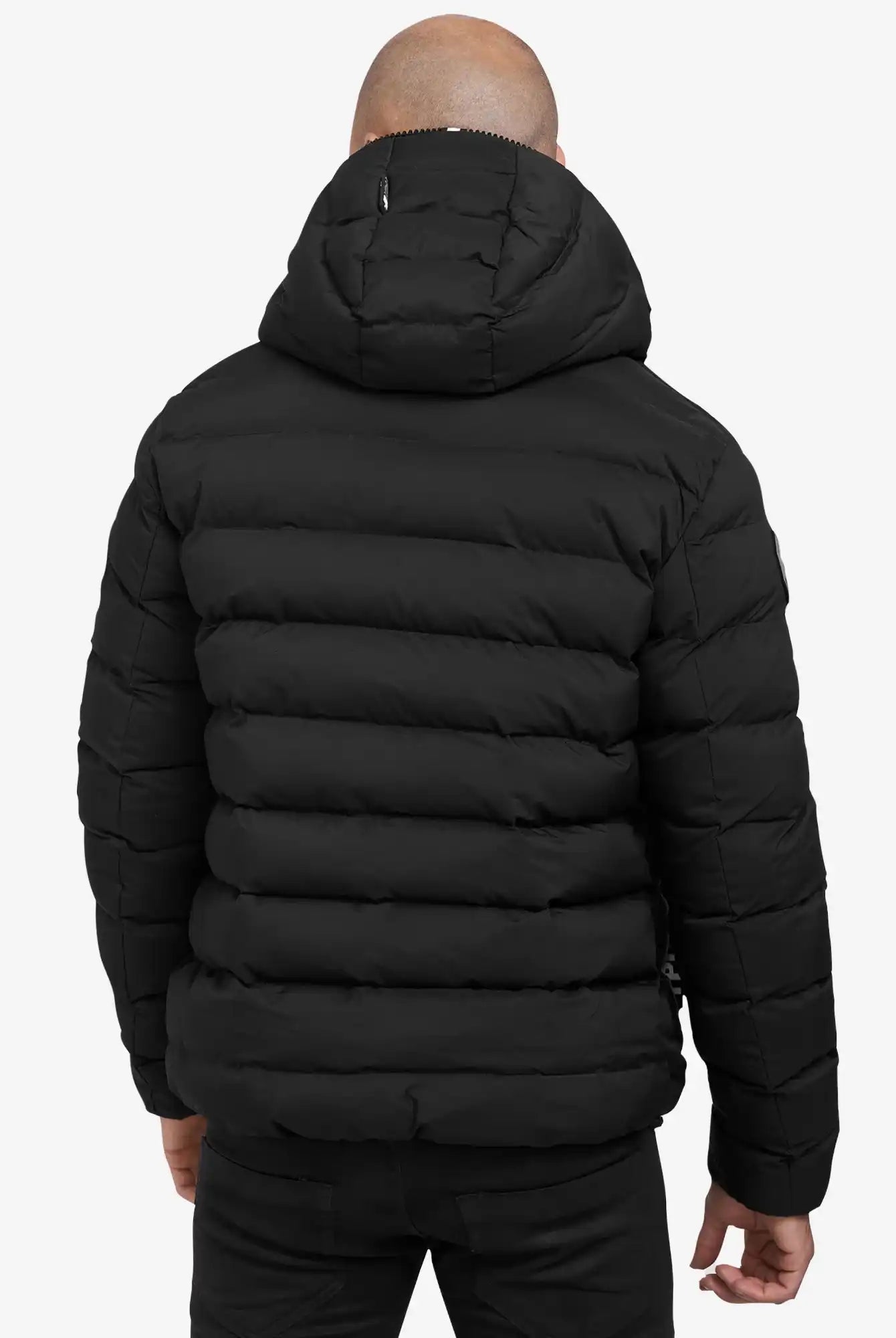 Eine Person trägt die Neo Kurze Pufferjacke mit Logo von trueprodigy in Schwarz, wasserabweisend und mit Kapuze. Die horizontale Steppung ist sichtbar, die Person steht entspannt mit den Armen an den Seiten, von hinten gesehen.