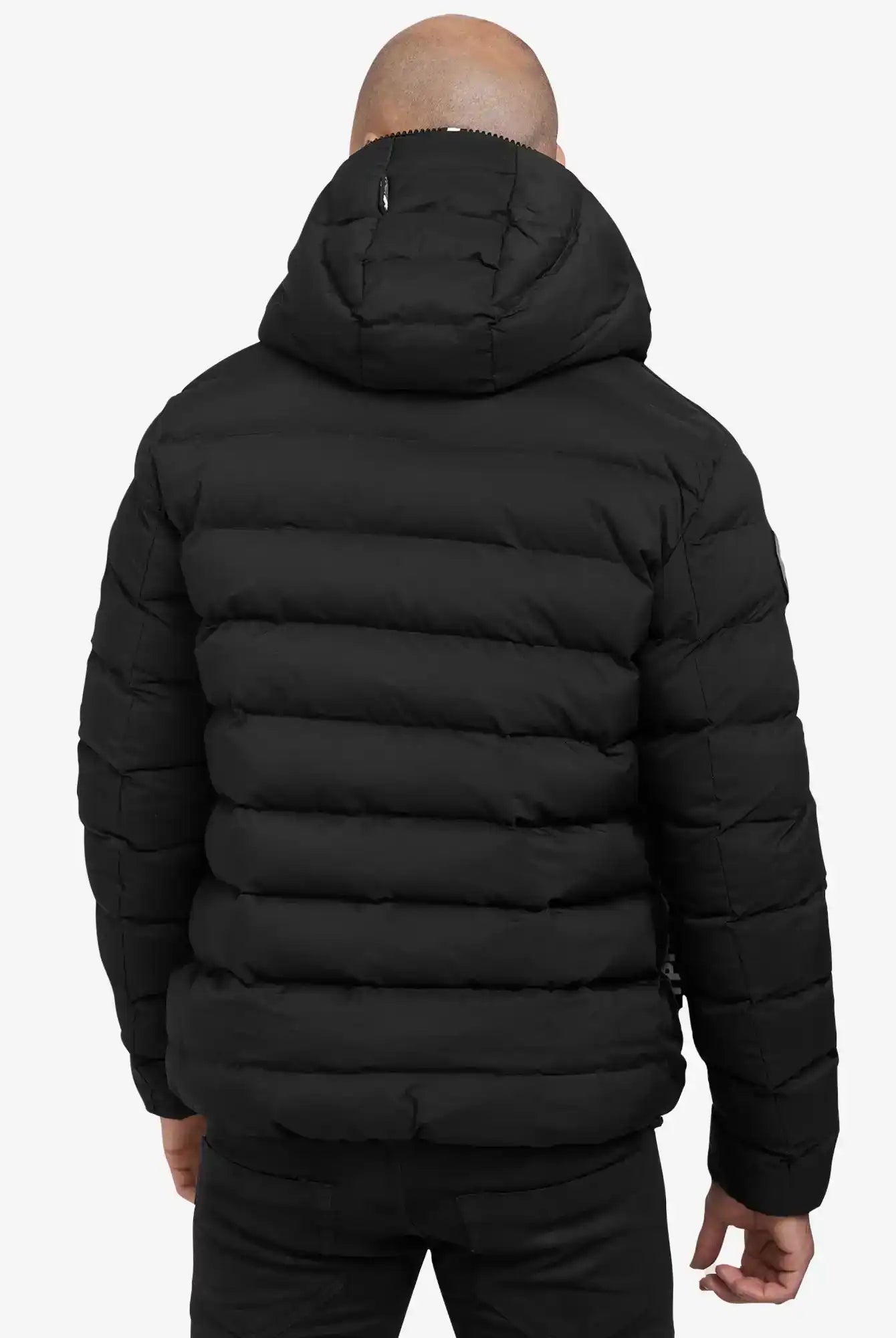 Eine Person trägt die Neo Kurze Pufferjacke mit Logo von trueprodigy in Schwarz, wasserabweisend und mit Kapuze. Die horizontale Steppung ist sichtbar, die Person steht entspannt mit den Armen an den Seiten, von hinten gesehen.