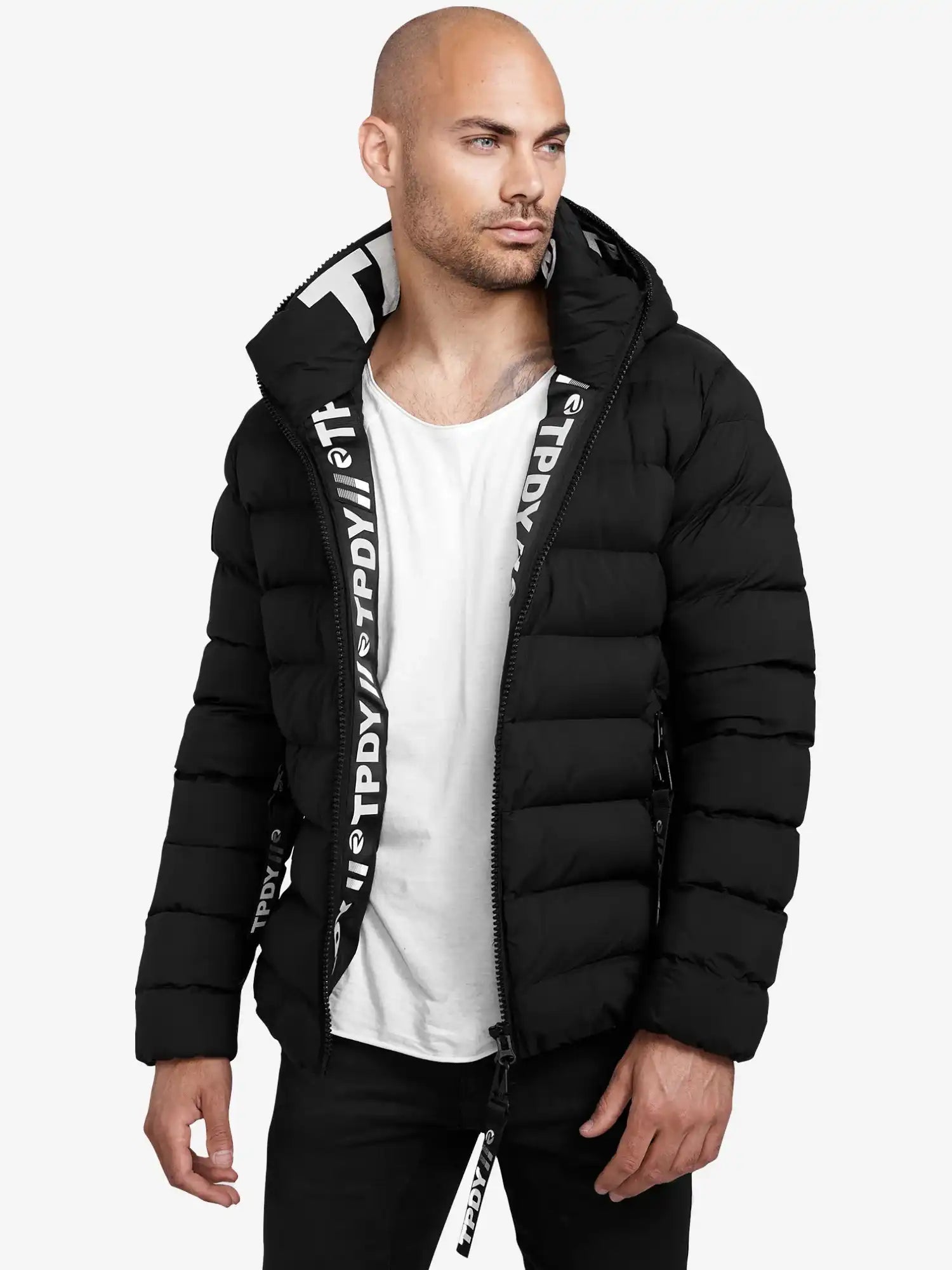 Ein Mann trägt eine schwarze Neo Kurze Pufferjacke mit Logo von trueprodigy mit Kapuze, dazu ein weißes T-Shirt und schwarze Hose, steht vor weißem Hintergrund und blickt nach links.