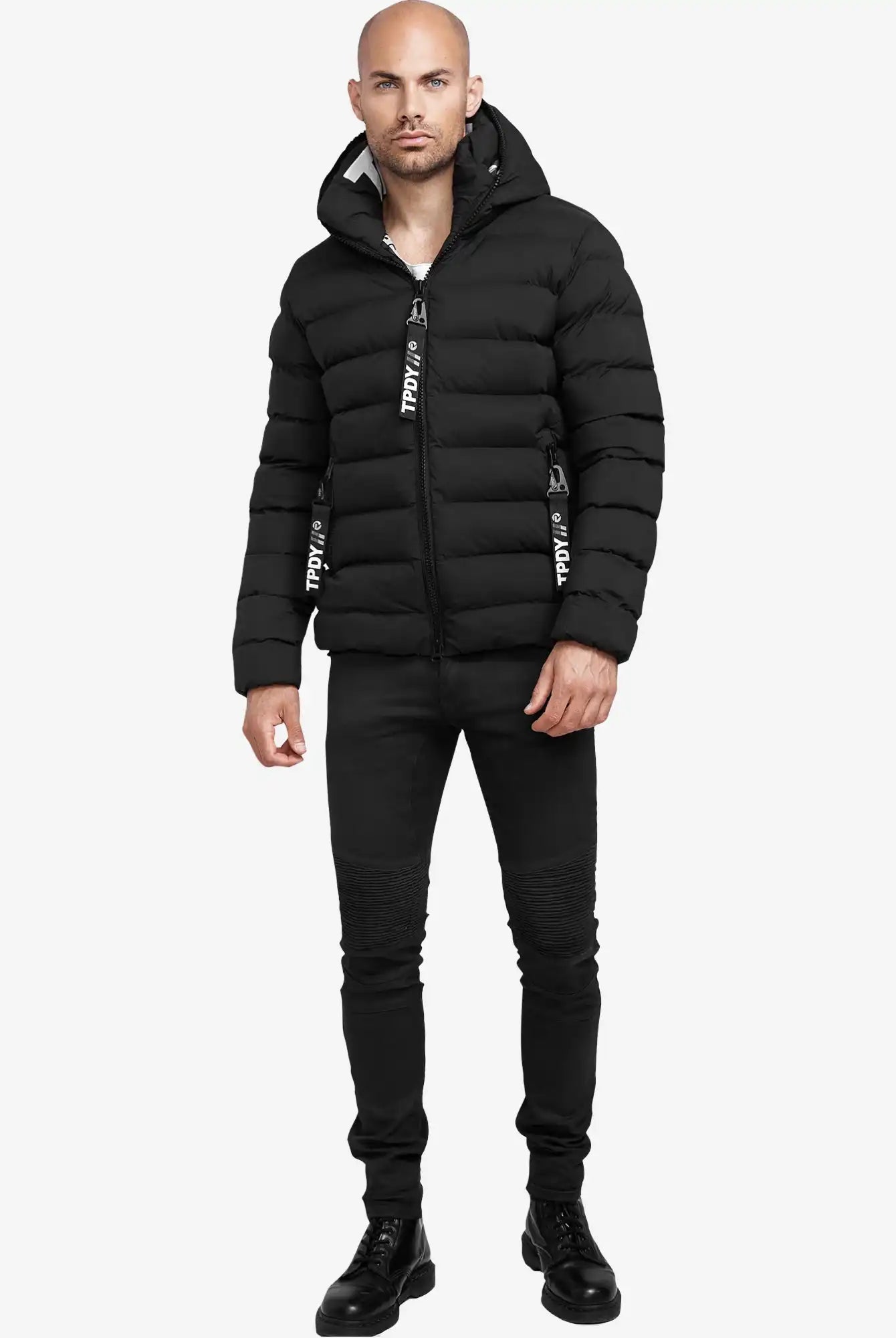 Ein Mann trägt die schwarze Neo Kurze Pufferjacke mit Logo von trueprodigy, schwarze Jeans und Schnürstiefel. Die wasserabweisende Jacke hat sichtbare Reißverschlüsse. Der Hintergrund ist schlicht weiß.