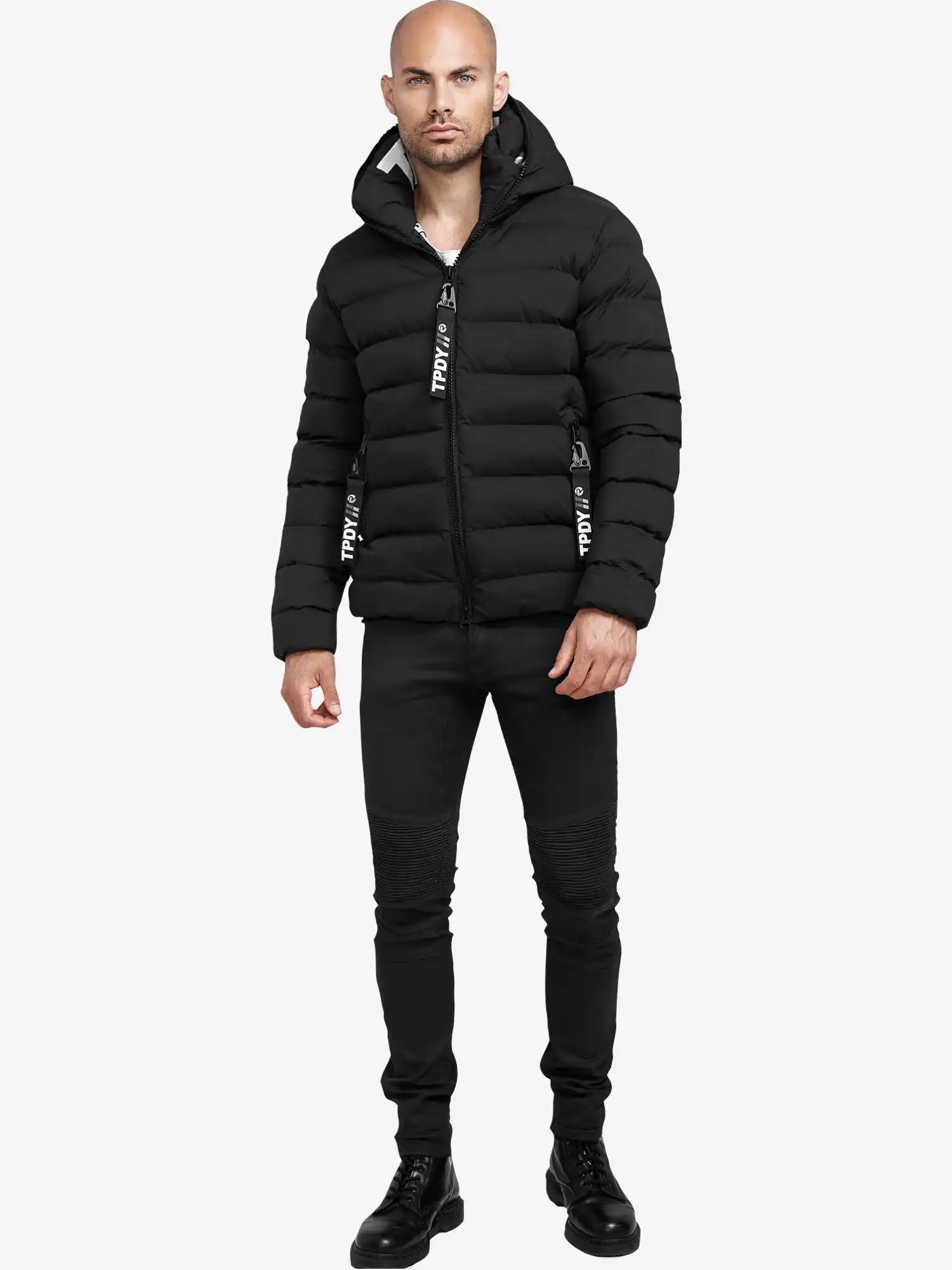 Ein Mann trägt die schwarze Neo Kurze Pufferjacke mit Logo von trueprodigy, schwarze Jeans und Schnürstiefel. Die wasserabweisende Jacke hat sichtbare Reißverschlüsse. Der Hintergrund ist schlicht weiß.