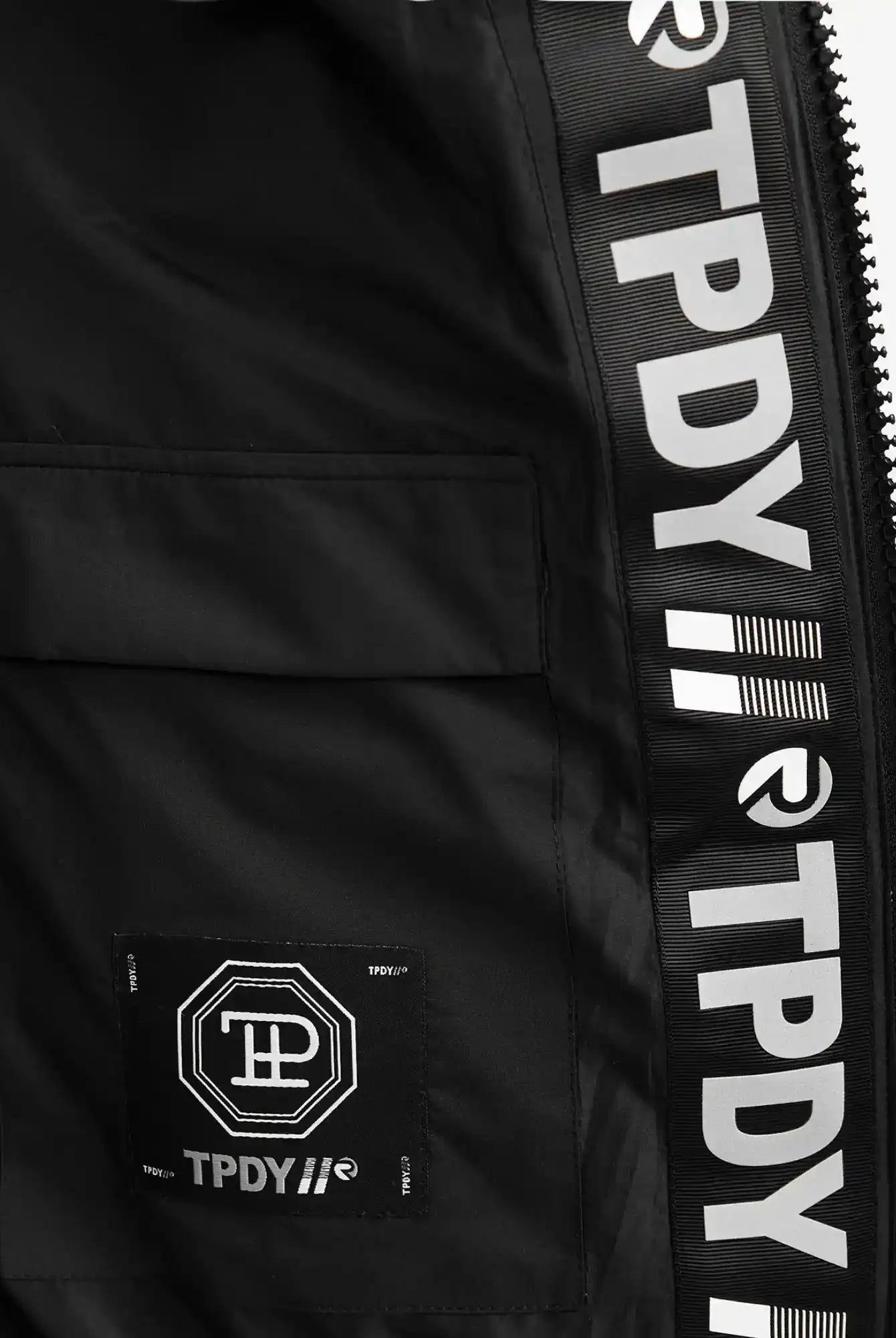 Nahaufnahme des Innenfutters der schwarzen Neo F Kurze Pufferjacke mit Logo von trueprodigy. Sie zeigt ein auffälliges weißes TP DY-Branding, geometrische Logos, eine rechteckige Innentasche und einen Hauch von Kapuzenstil.