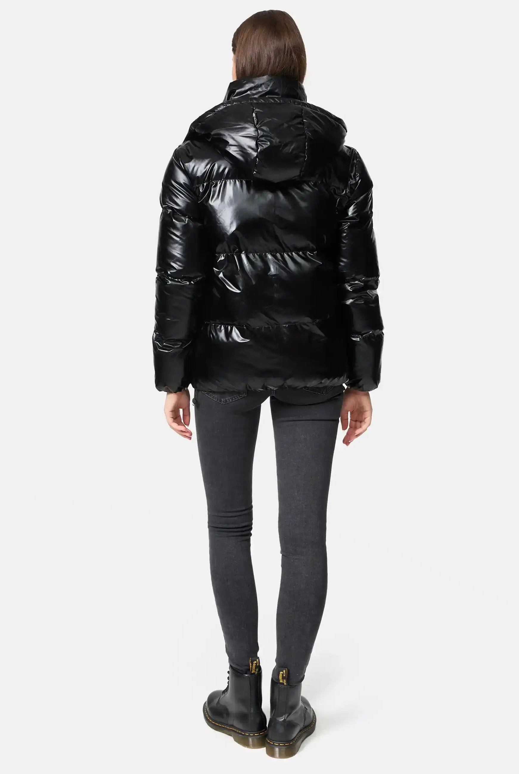 Frau trägt TRUEPRODIGY constance schwarze Steppjacke, Schriftzug „TRUEDPDE“, kombiniert mit schwarzen Jeans und Stiefeln. Jacke glänzend, elegant, wintertauglich, urbaner Stil.