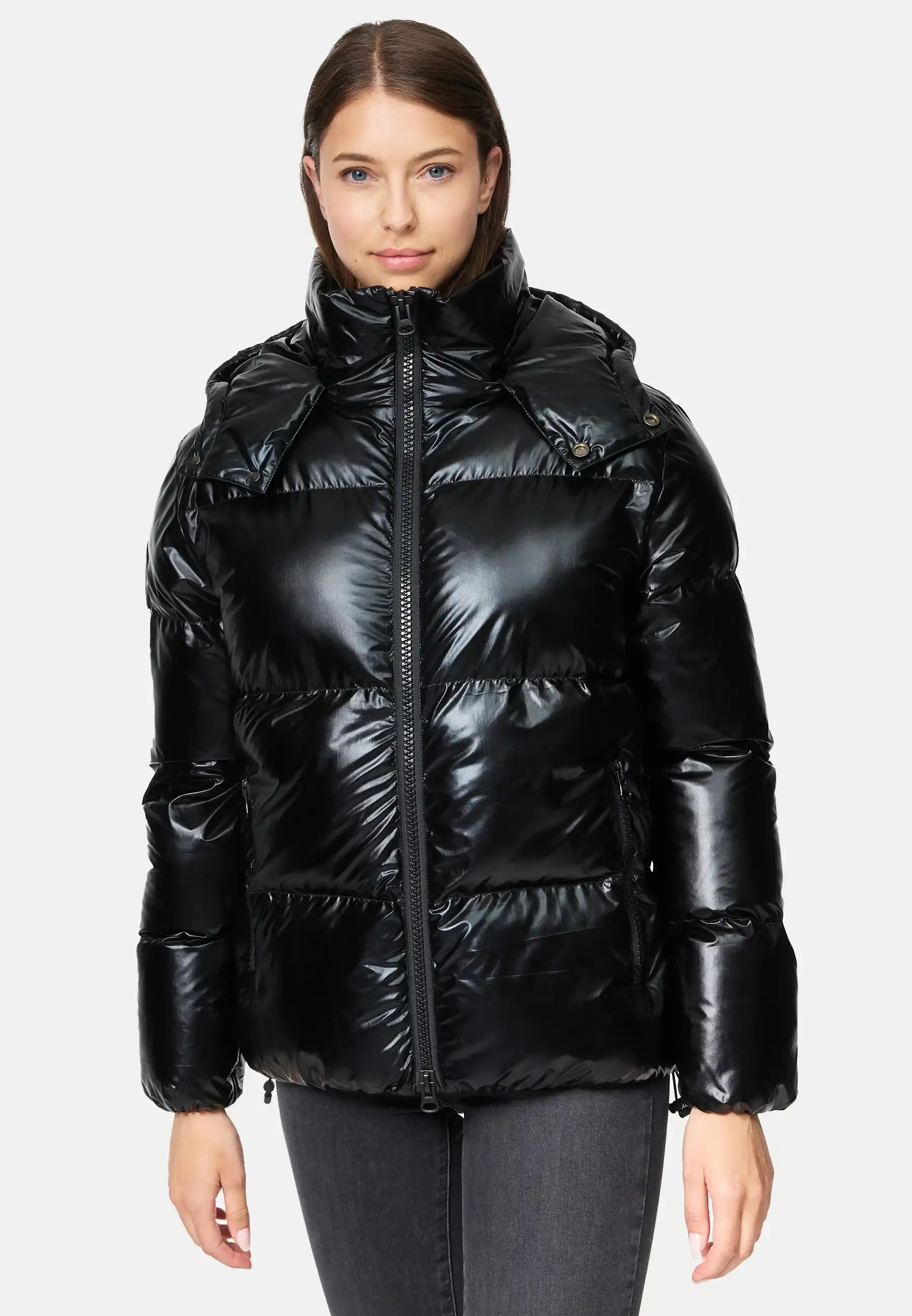 Eine Person steht mit dem Gesicht nach vorne und trägt die trueprodigy Constance F Glänzende Winterjacke mit Kapuze - eine glänzende schwarze Puffjacke mit hohem Kragen und Kapuze, die mit einer dunkelgrauen Jeans vor einem schlichten, hellen Hintergrund kombiniert wird.