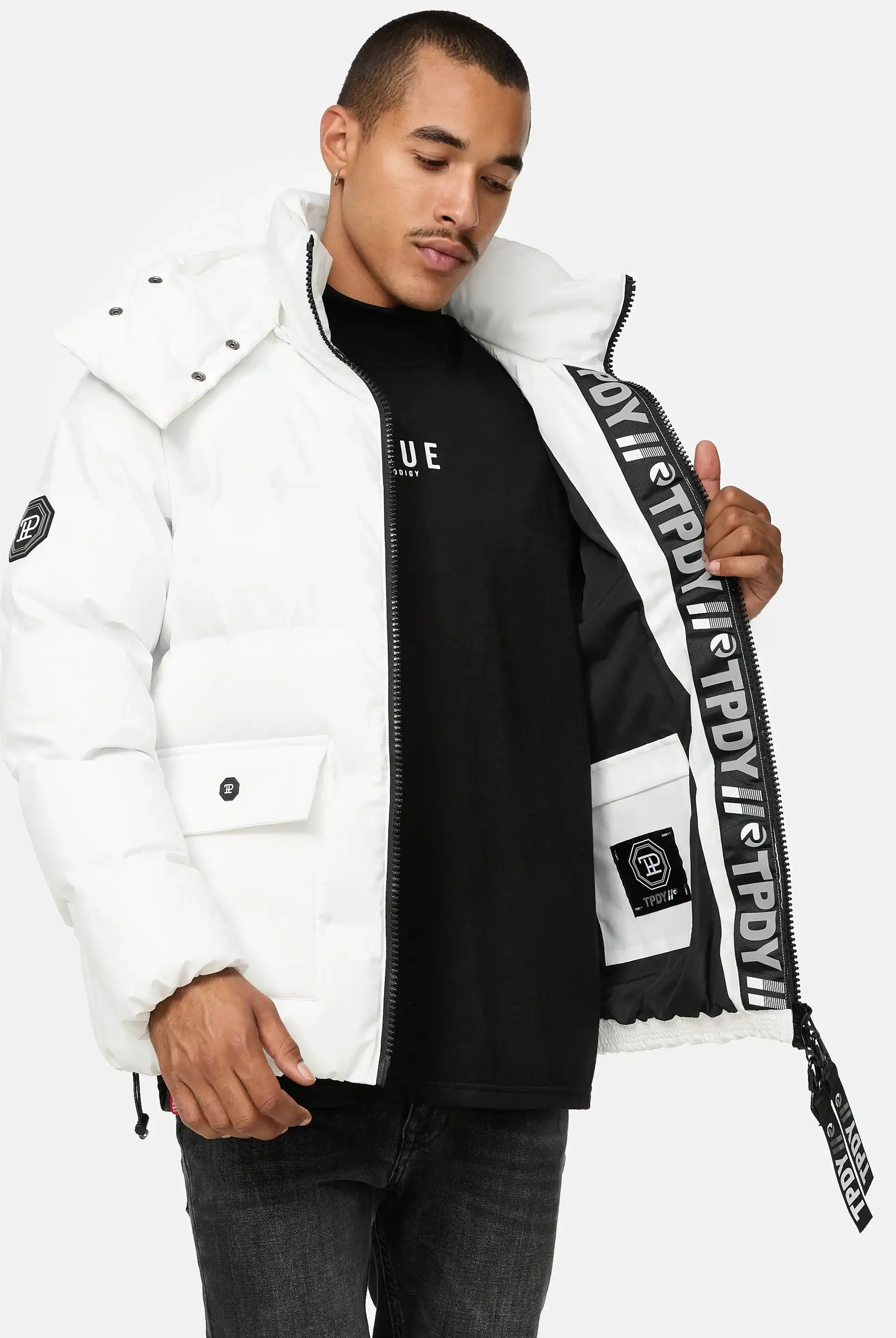 Ein Mann modelliert die trueprodigy Franco Winterjacke mit abnehmbarer Kapuze, eine weiße Pufferjacke mit abnehmbarer Kapuze, und hält sie offen, um das schwarz-weiße Markenfutter zu zeigen - eine auffällige reflektierende Winterjacke für einen mutigen Stil.