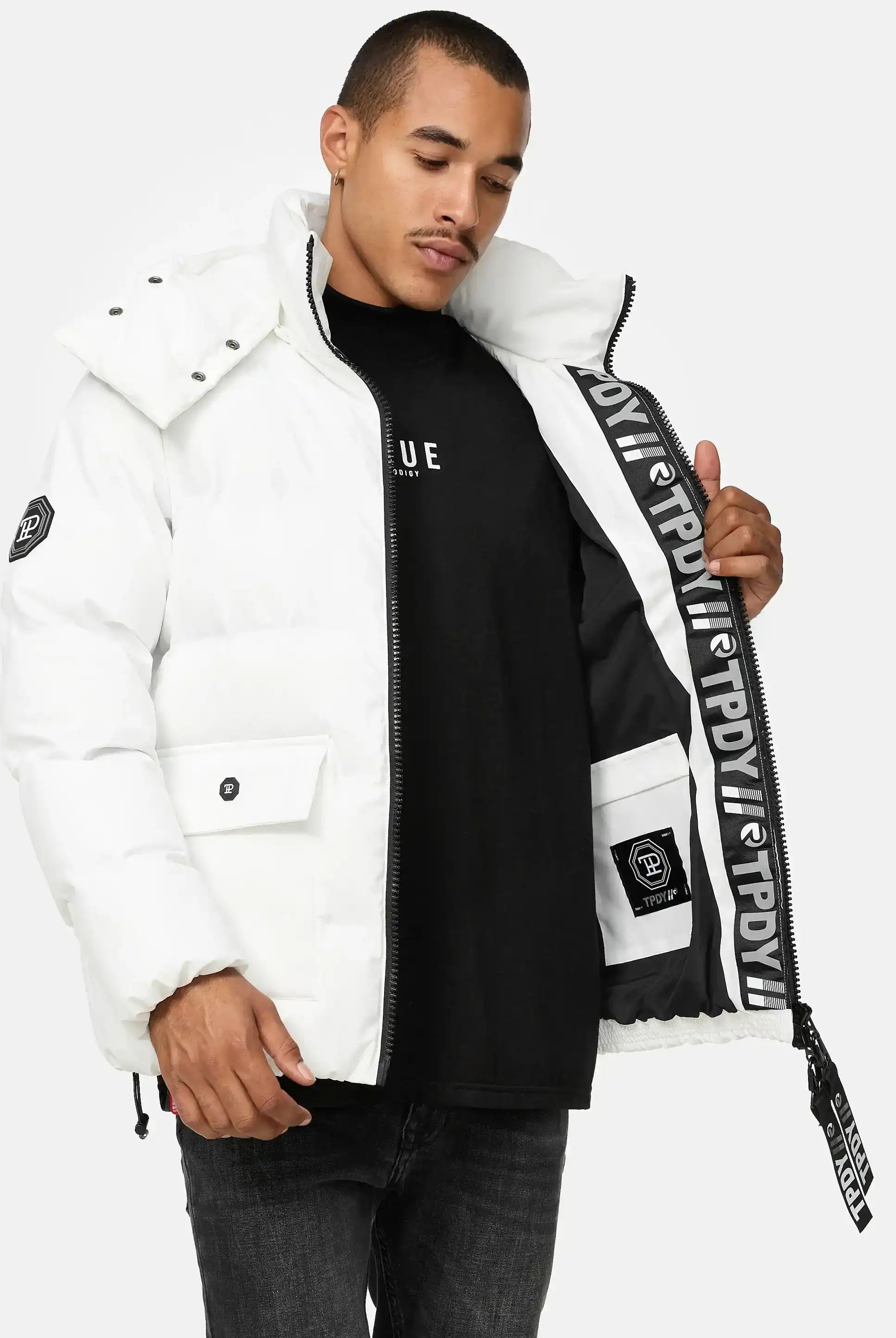 Ein Mann modelliert die trueprodigy Franco Winterjacke mit abnehmbarer Kapuze, eine weiße Pufferjacke mit abnehmbarer Kapuze, und hält sie offen, um das schwarz-weiße Markenfutter zu zeigen - eine auffällige reflektierende Winterjacke für einen mutigen Stil.
