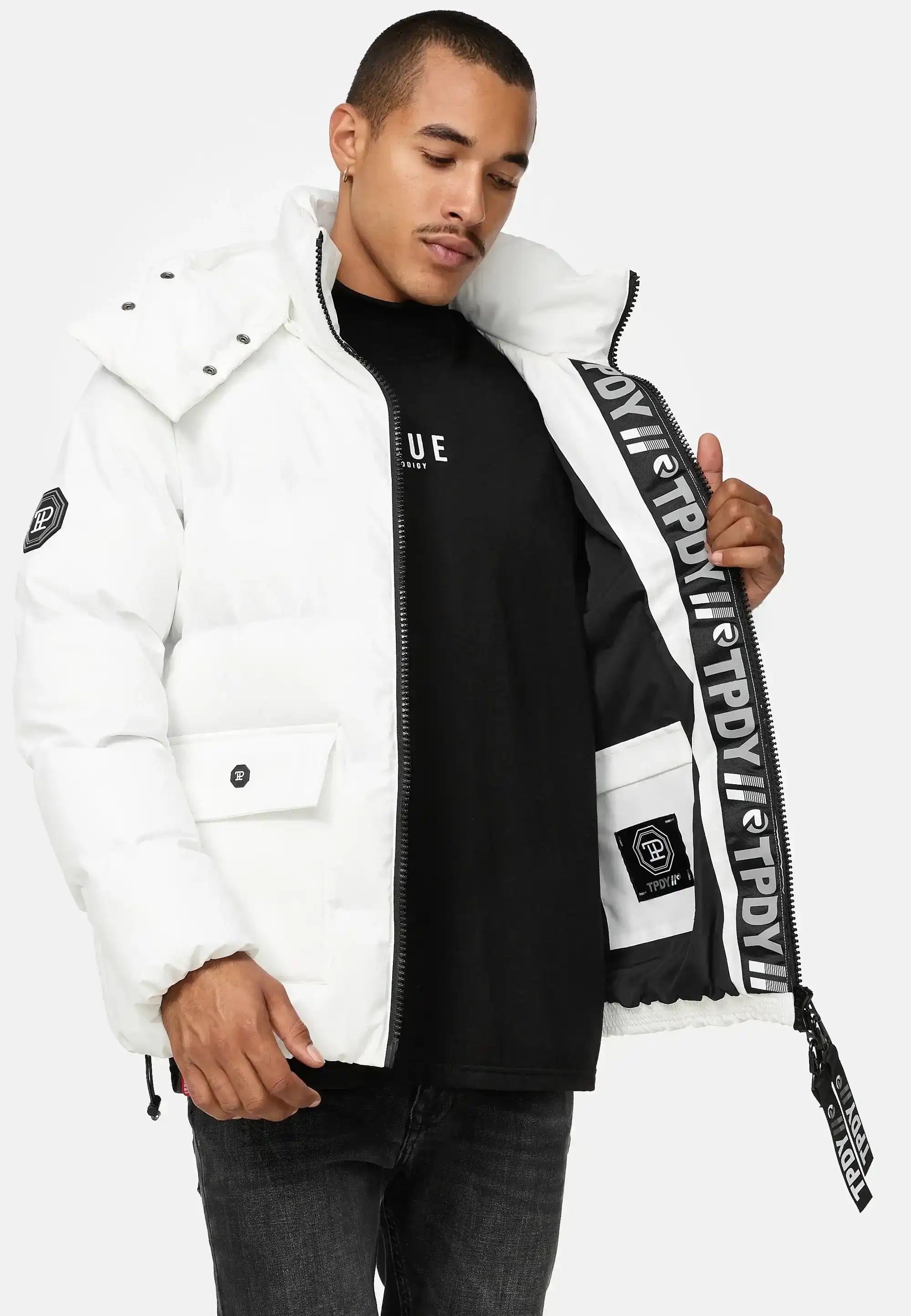 Ein Mann modelliert die trueprodigy Franco Winterjacke mit abnehmbarer Kapuze, eine weiße Pufferjacke mit abnehmbarer Kapuze, und hält sie offen, um das schwarz-weiße Markenfutter zu zeigen - eine auffällige reflektierende Winterjacke für einen mutigen Stil.