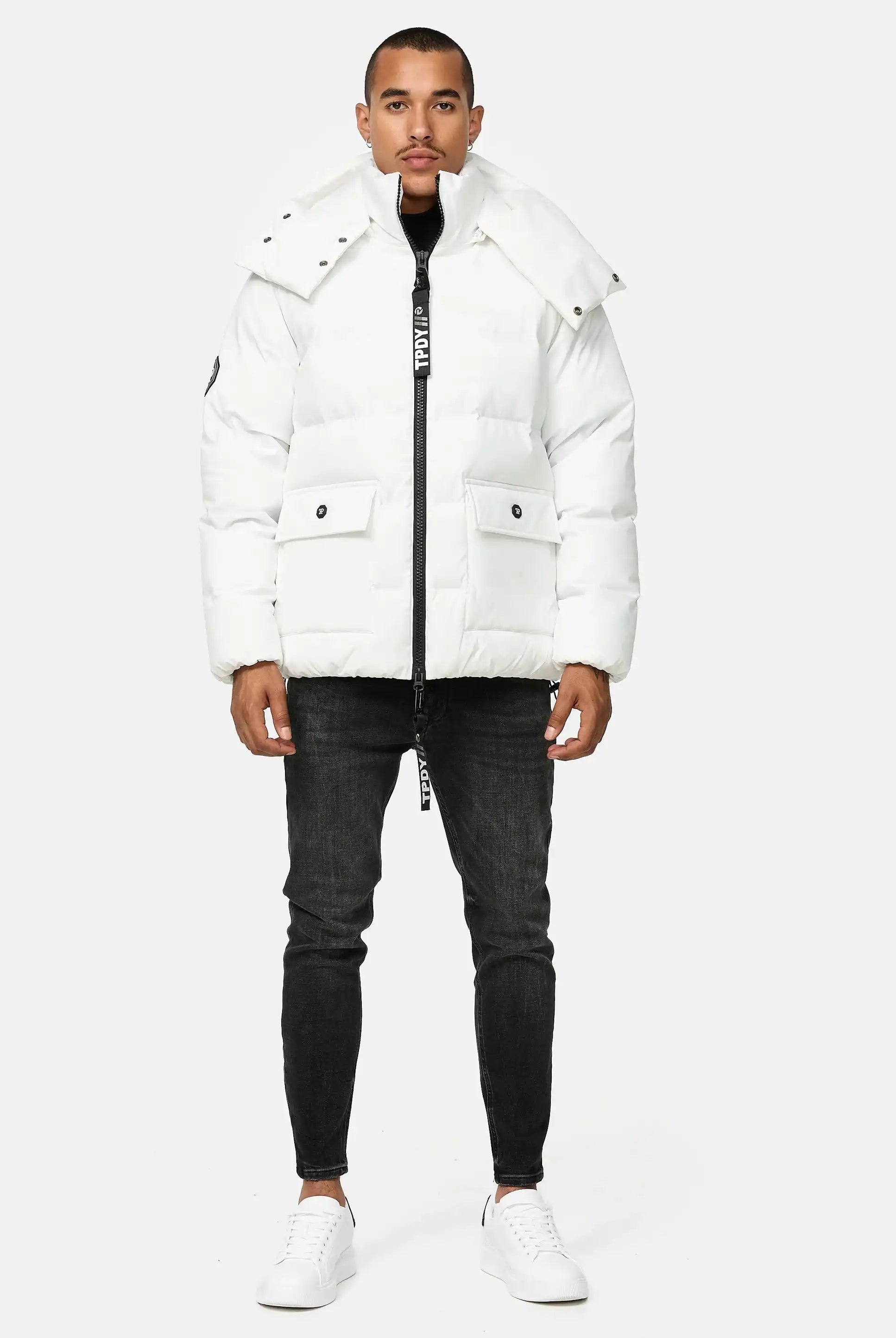 Ein Mann steht vor einem hellgrauen Hintergrund. Er trägt die trueprodigy Franco Winterjacke mit abnehmbarer Kapuze, schwarze Skinny Jeans und weiße Turnschuhe.