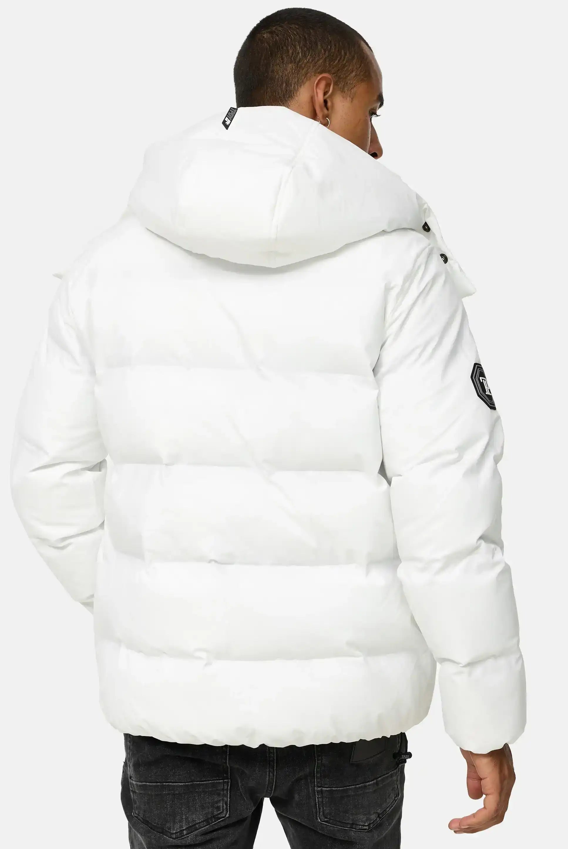 Eine Person, die die trueprodigy Franco Winterjacke mit abnehmbarer Kapuze in Weiß mit einem Aufnäher auf dem linken Ärmel trägt, steht mit dem Rücken zur Kamera und kombiniert sie mit einer schwarzen Jeans.