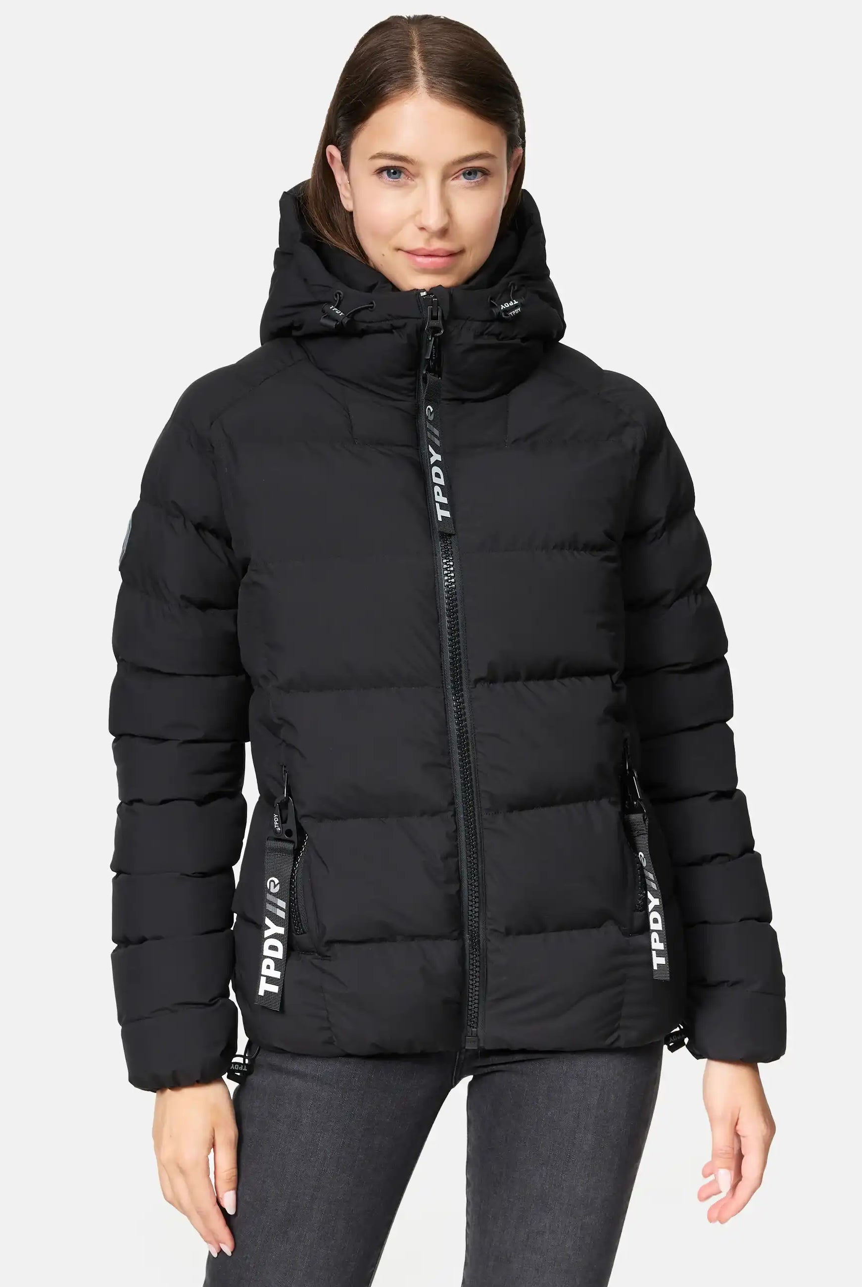 Eine Person trägt die Murphy F Matte Steppjacke mit Kapuze von trueprodigy in Schwarz mit Frontreißverschluss und zwei Taschen. Die wasserabweisende Jacke zeigt einen TPDY-Aufdruck vor hellem, schlichten Hintergrund.