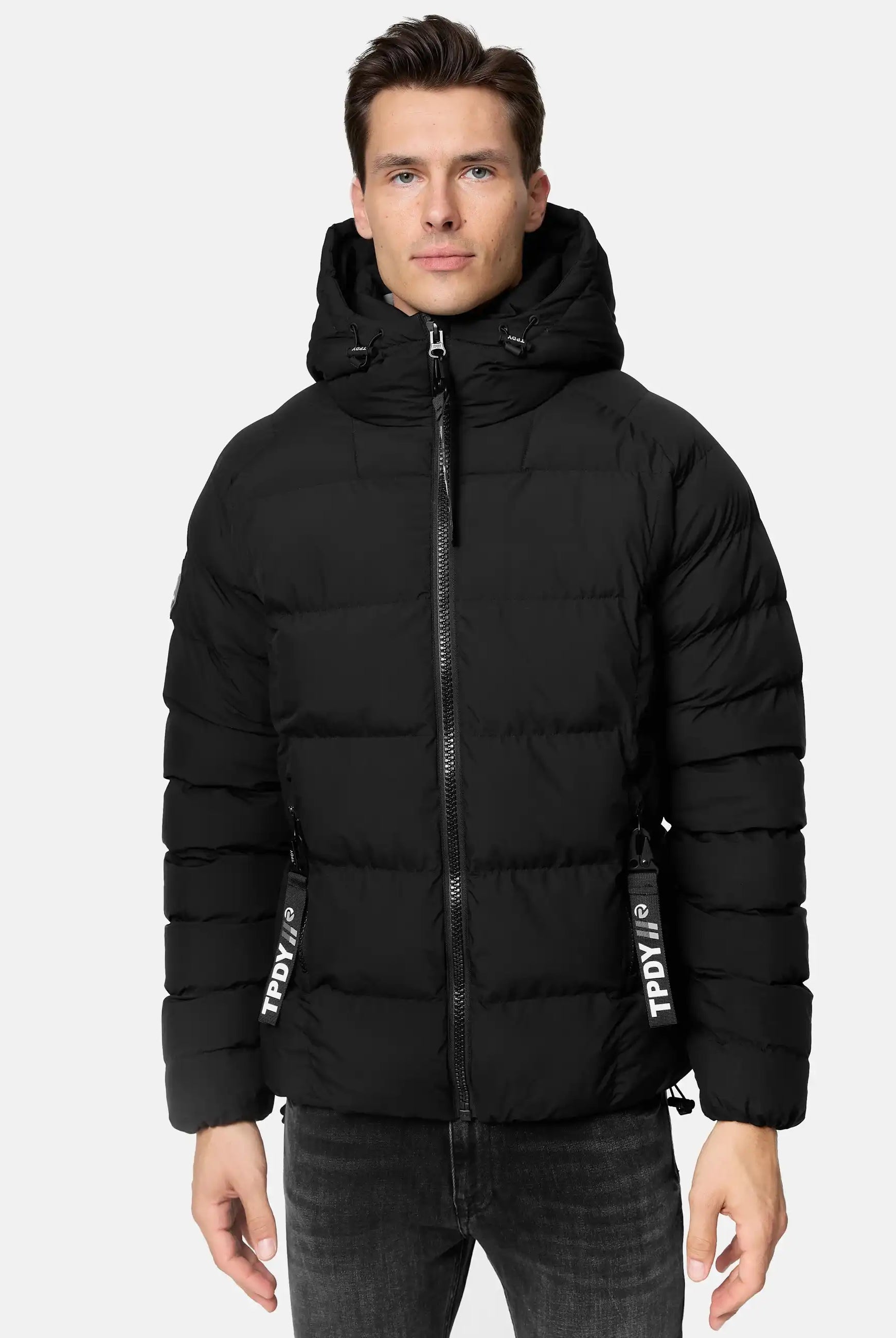 Ein Mann trägt die Murphy Matte Steppjacke mit Kapuze von trueprodigy in Schwarz mit wasserabweisendem Material, Frontreißverschluss, zwei Reißverschlusstaschen und horizontalen Steppnähten zu dunklen Jeans vor hellem, schlichtem Hintergrund.