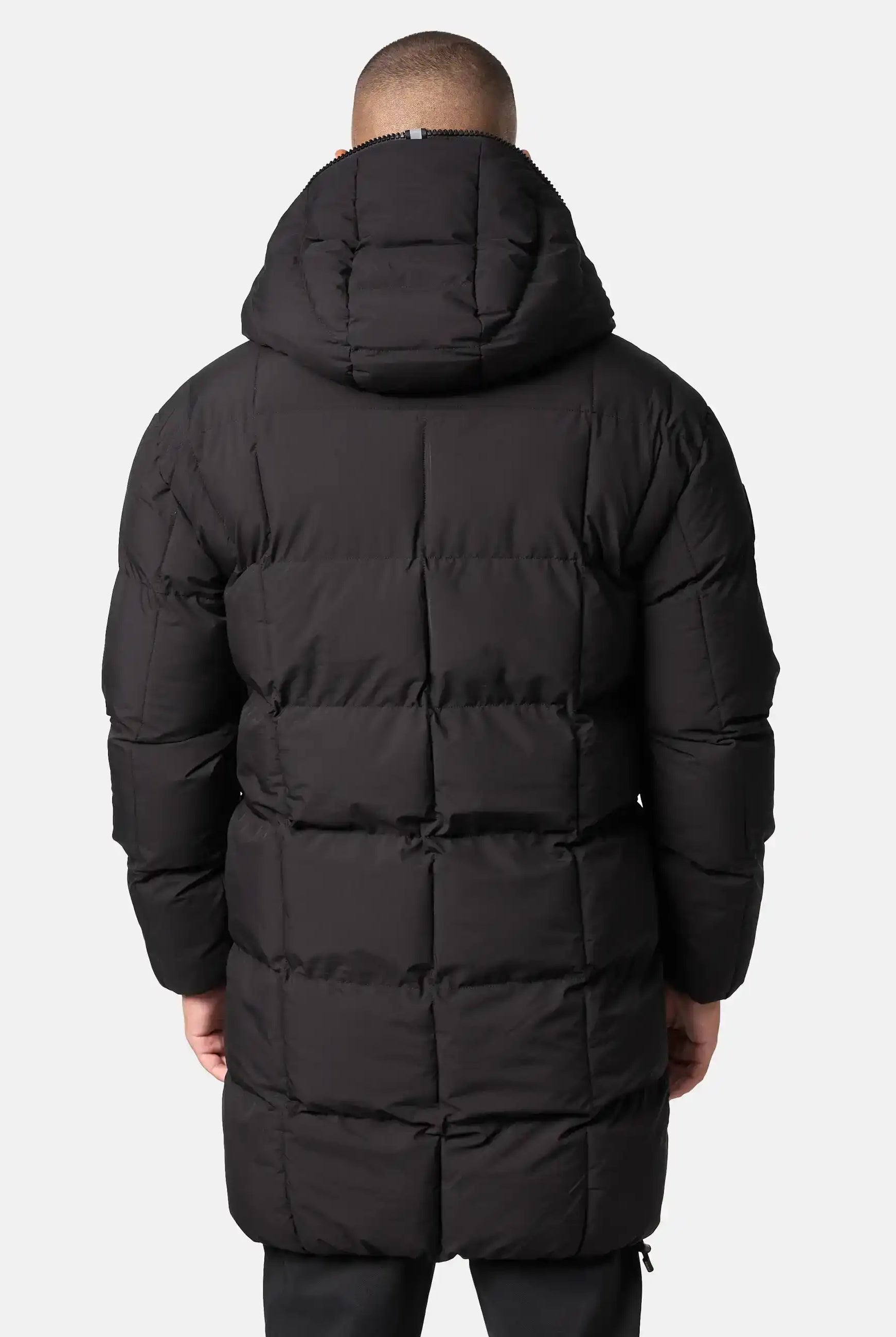 Eine Person, die die von hinten gezeigte Trueprodigy Willo Lange Pufferjacke mit Kapuze trägt, steht vor einem schlichten hellgrauen Hintergrund.