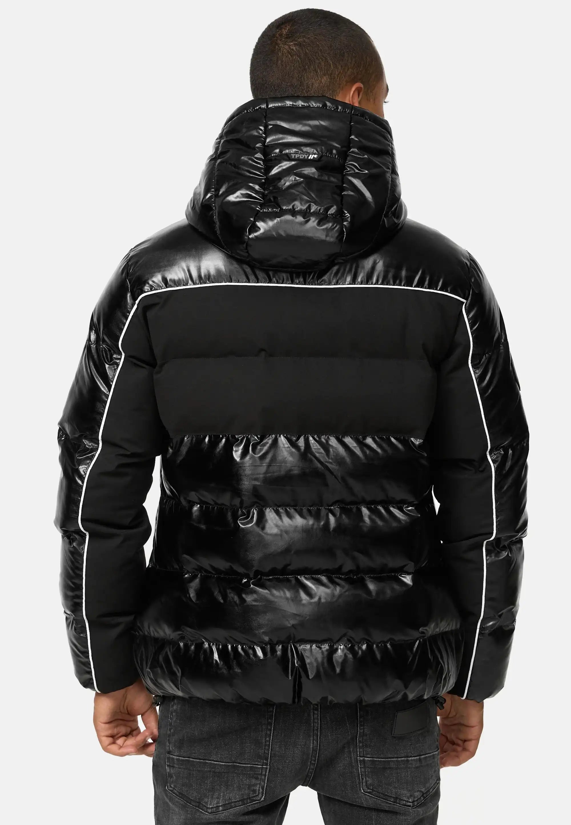 Man sieht eine Person von hinten, die die trueprodigy Clark Winterjacke mit Kapuze und Logo trägt, eine glänzende schwarze Jacke mit weißen Paspelierungen. Diese gesteppte Winterjacke lässt sich stilvoll mit dunklen Jeans kombinieren und sorgt für einen eleganten Winterlook.