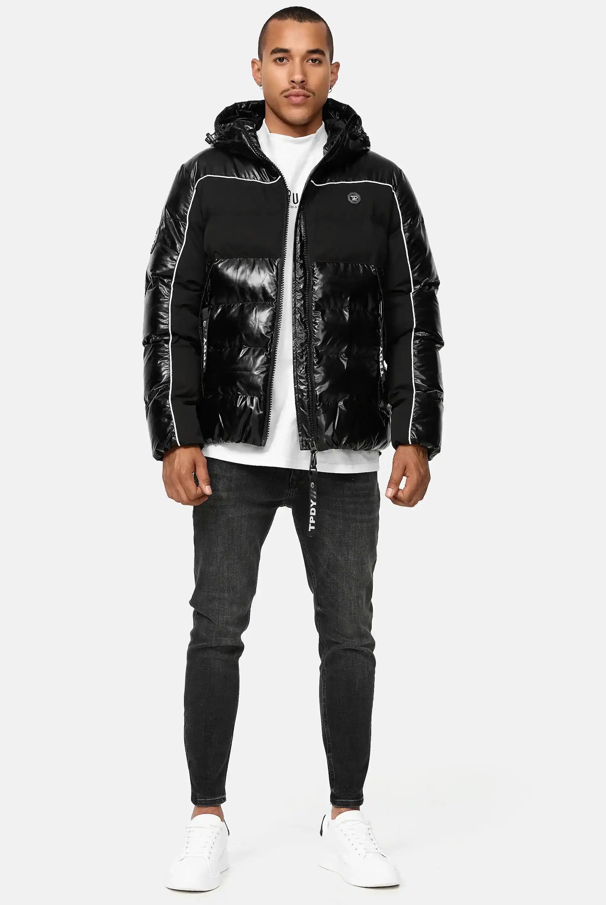 Ein Mann steht mit dem Gesicht nach vorne und trägt die trueprodigy Clark Winterjacke mit Kapuze und Logo, ein weißes T-Shirt, dunkle Skinny Jeans und weiße Turnschuhe vor einem schlichten hellen Hintergrund.