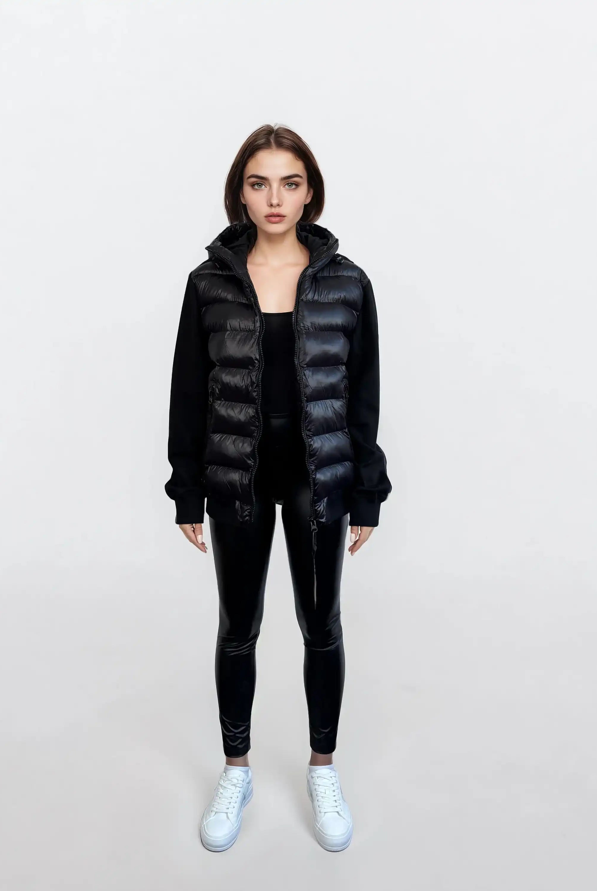 Eine Frau steht vor weißem Hintergrund und trägt eine Oversized Damen Bomber Jacke im urbanen Materialmix-Design von trueprodigy über einem schwarzen Longsleeve, dazu schwarze Leggings und weiße Sneaker. Sie hat glattes braunes Haar und einen neutralen Blick.