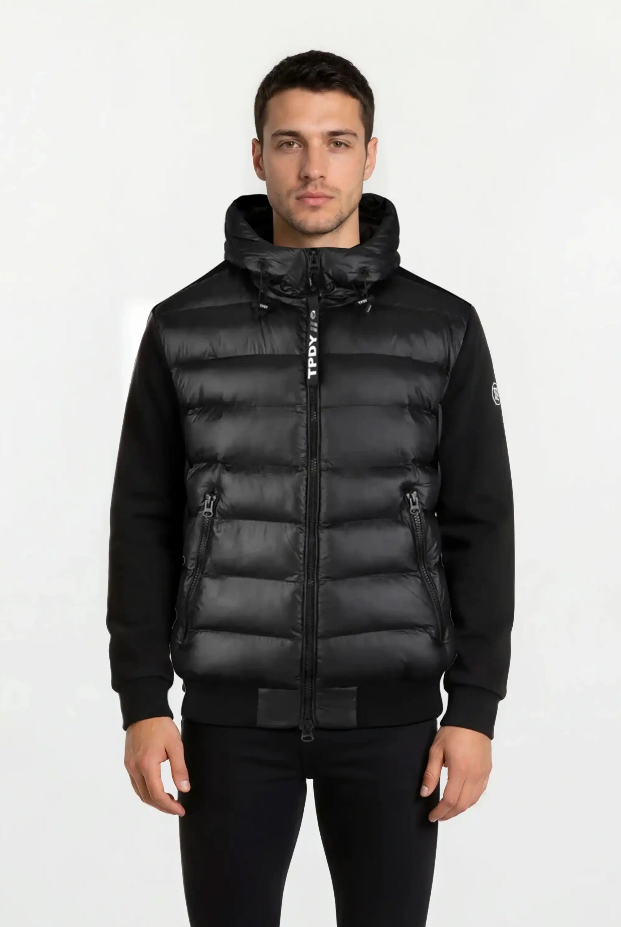 Ein Mann trägt eine schwarze, gesteppte Herren Übergangsjacke von trueprodigy mit Kapuze und zwei Reißverschlusstaschen - perfekt für urbanen City-Style. Die wasserabweisende Jacke hebt sich vor einem schlichten, hellen Hintergrund ab.