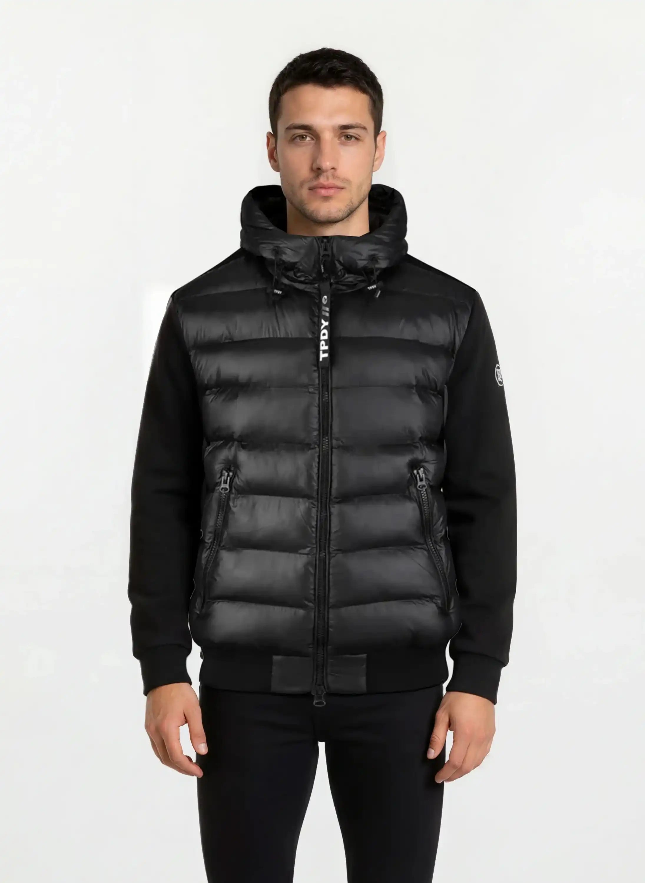 Ein Mann trägt eine schwarze, gesteppte Herren Übergangsjacke von trueprodigy mit Kapuze und zwei Reißverschlusstaschen - perfekt für urbanen City-Style. Die wasserabweisende Jacke hebt sich vor einem schlichten, hellen Hintergrund ab.